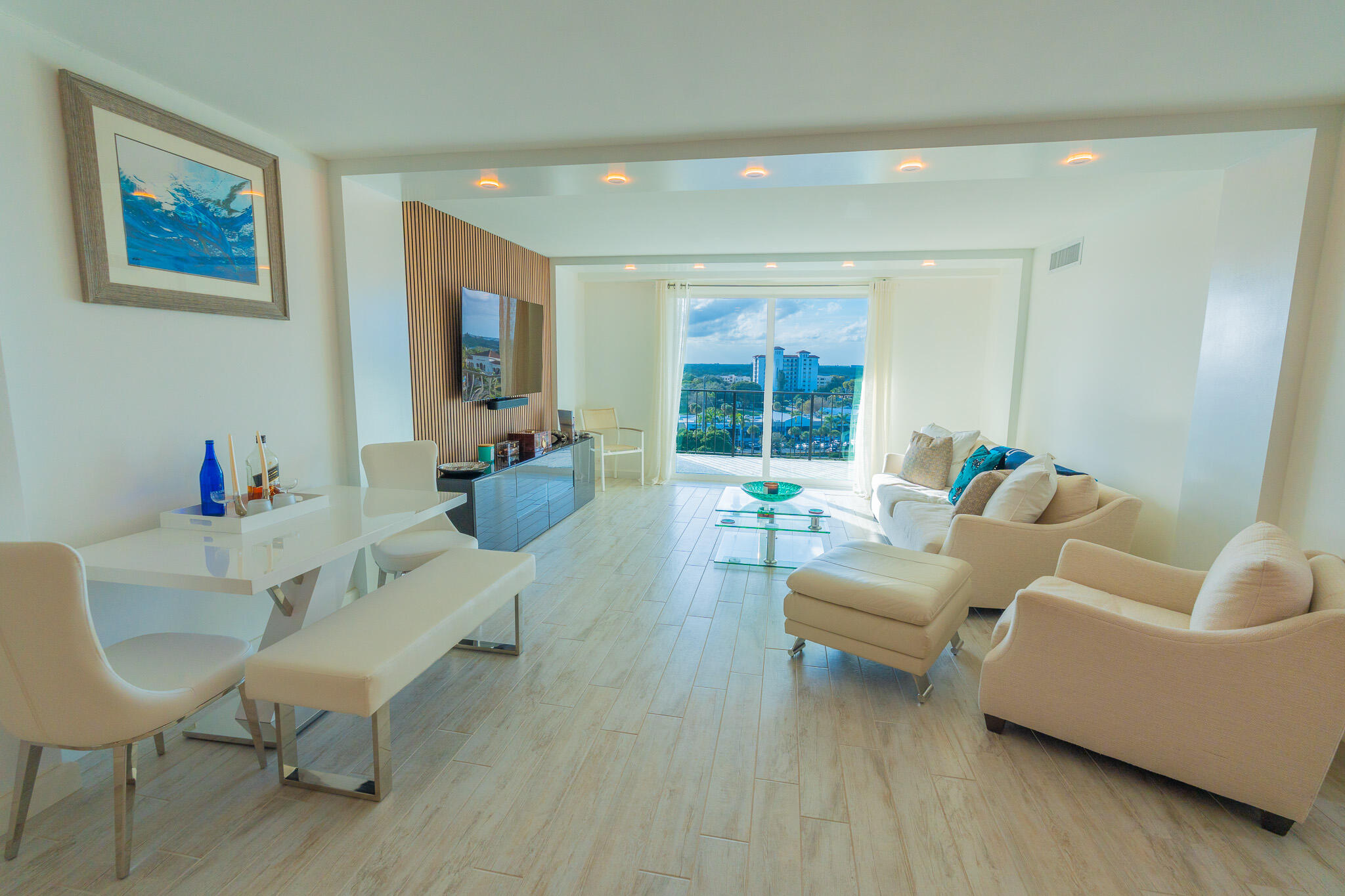 Bright living room with white seating and a balcony view of buildings and water.