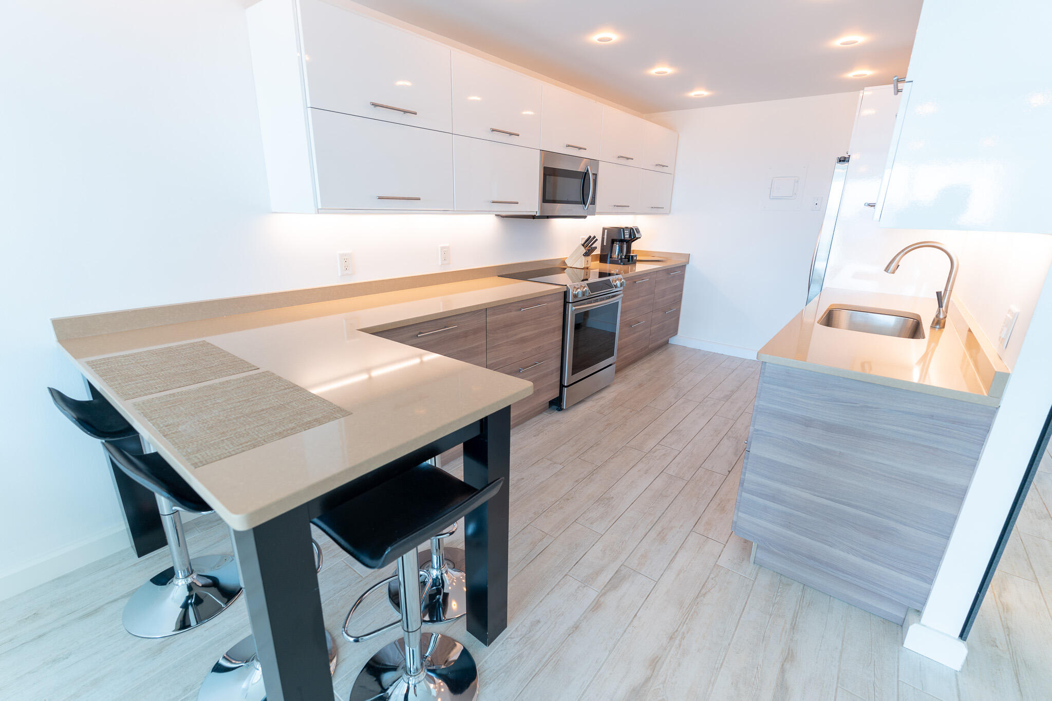 Modern condo kitchen with white cabinets, stainless appliances, and a breakfast bar with black stools.