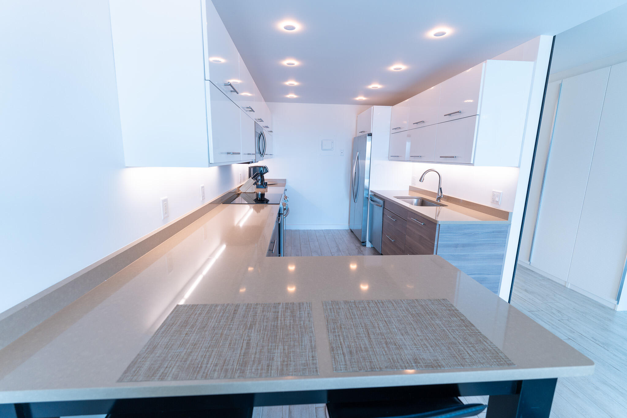 Modern kitchen with white cabinets, stainless-steel appliances, and a broad stone countertop.