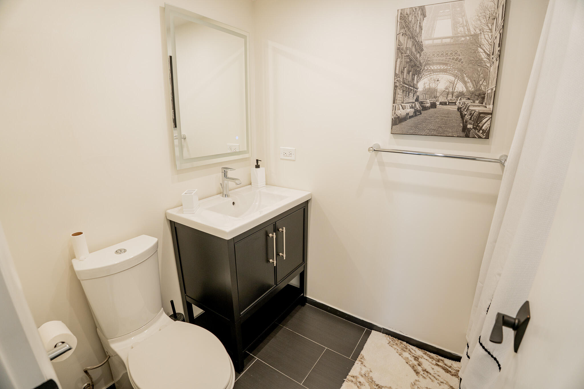 Bathroom with a dark vanity, white sink and toilet, and framed Eiffel Tower street scene.