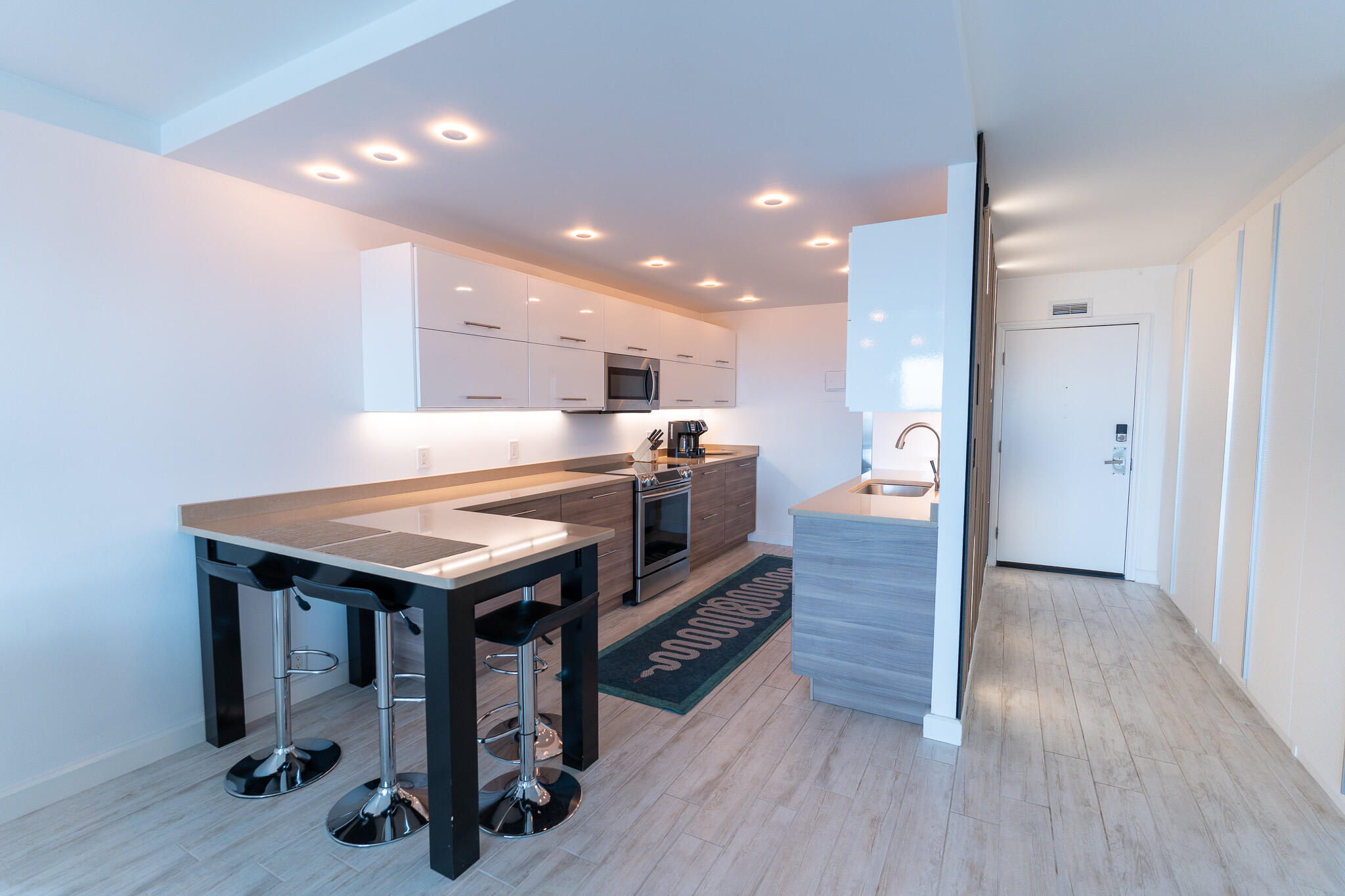 Modern kitchen with a breakfast bar, three stools, stainless steel appliances, and a sink peninsula.