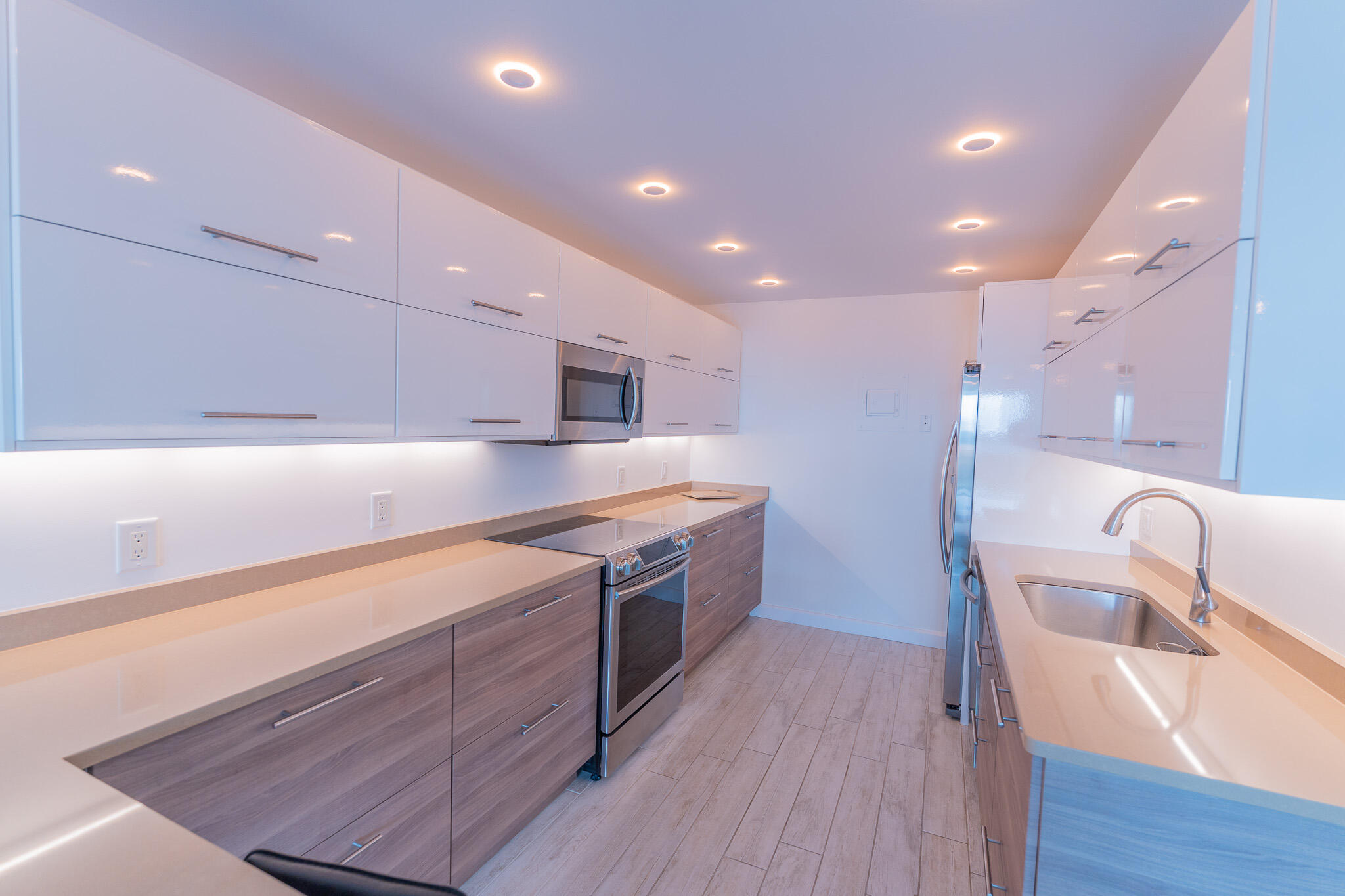 Modern galley kitchen with glossy white cabinets, gray wood cabinetry, and stainless steel appliances.