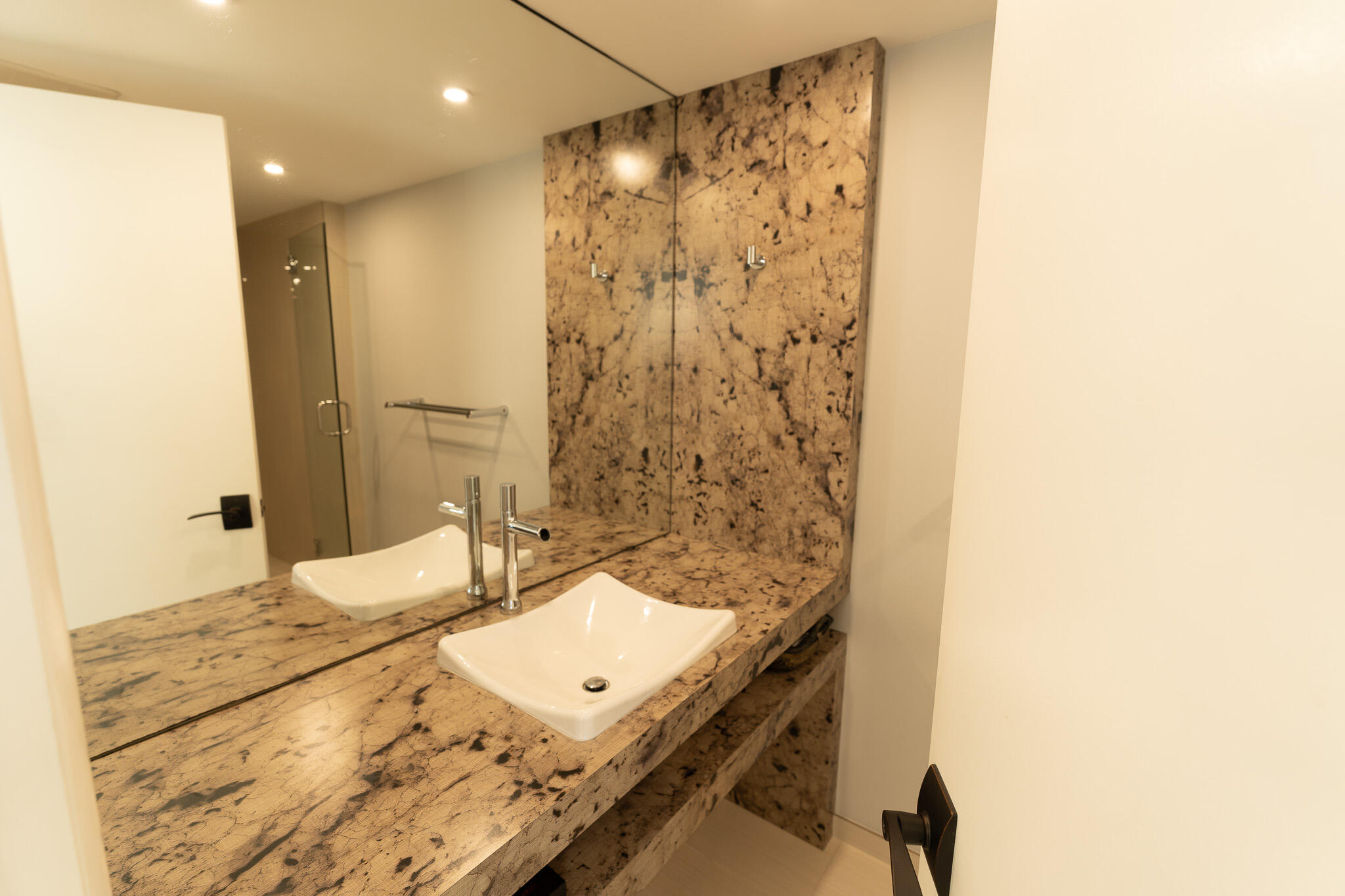 Bathroom vanity with a white vessel sink, chrome faucet, and dramatic patterned stone countertop and backsplash.