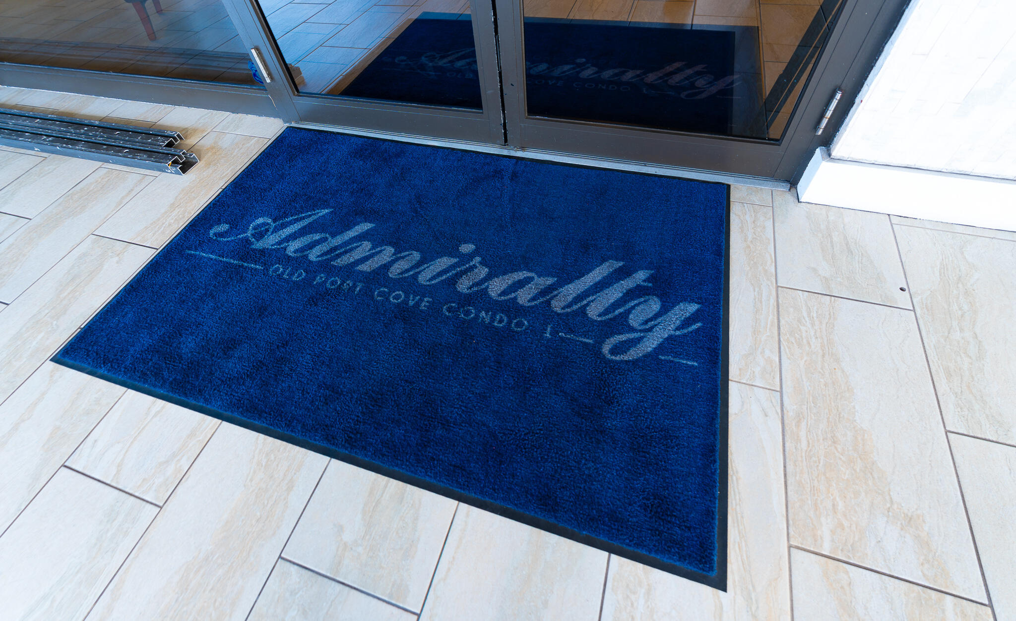 Condominium entrance with glass doors and a blue 1200 Marine Way doormat.