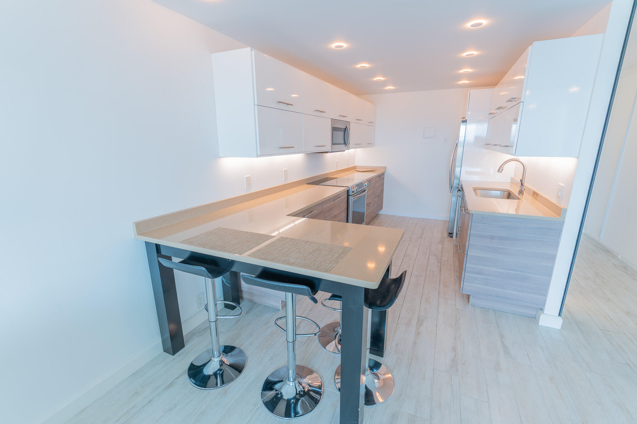 Modern white kitchen with a peninsula, chrome bar stools, and stainless steel appliances.