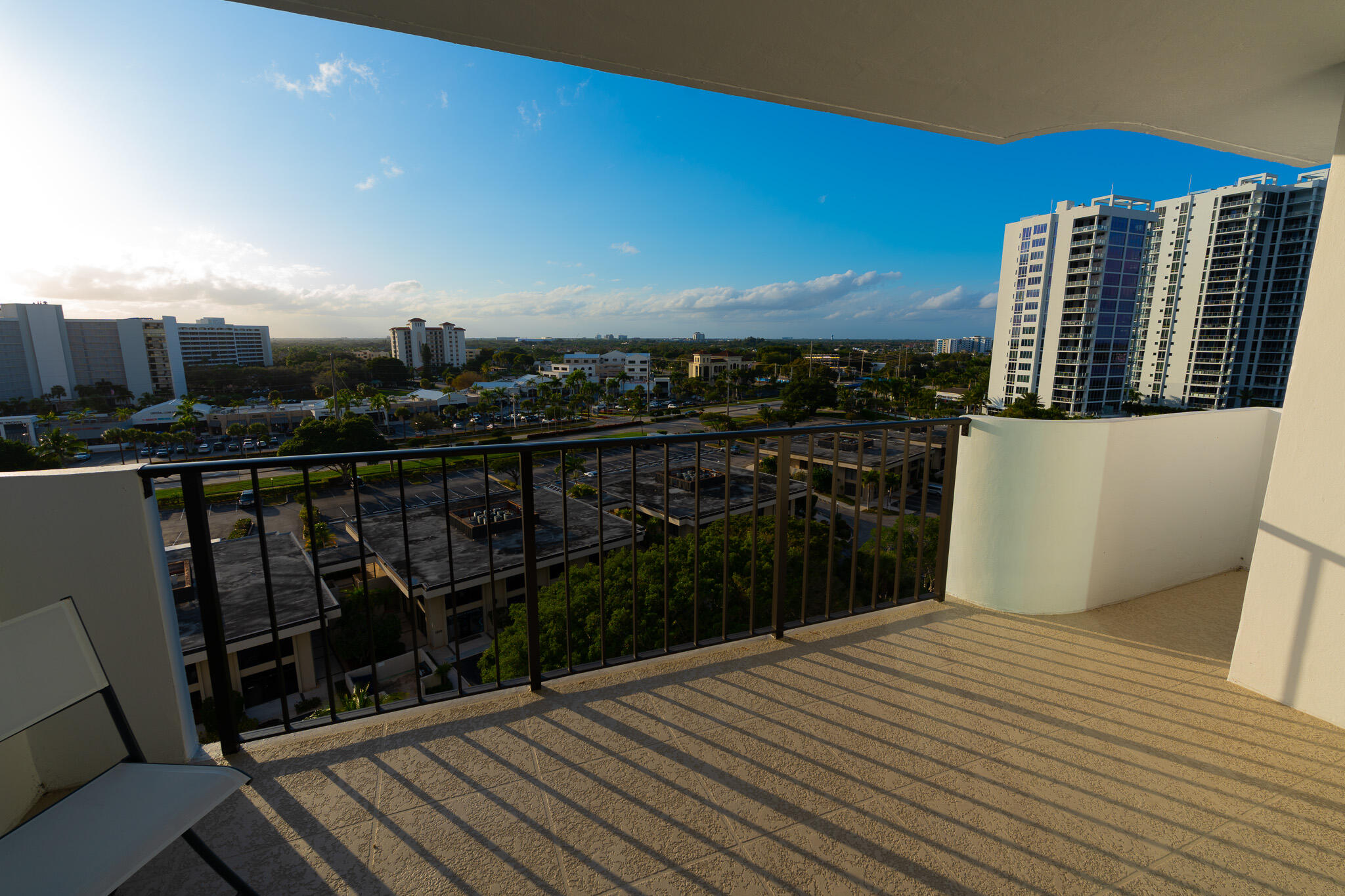 High-rise balcony overlooking nearby buildings, parking areas, and greenery.