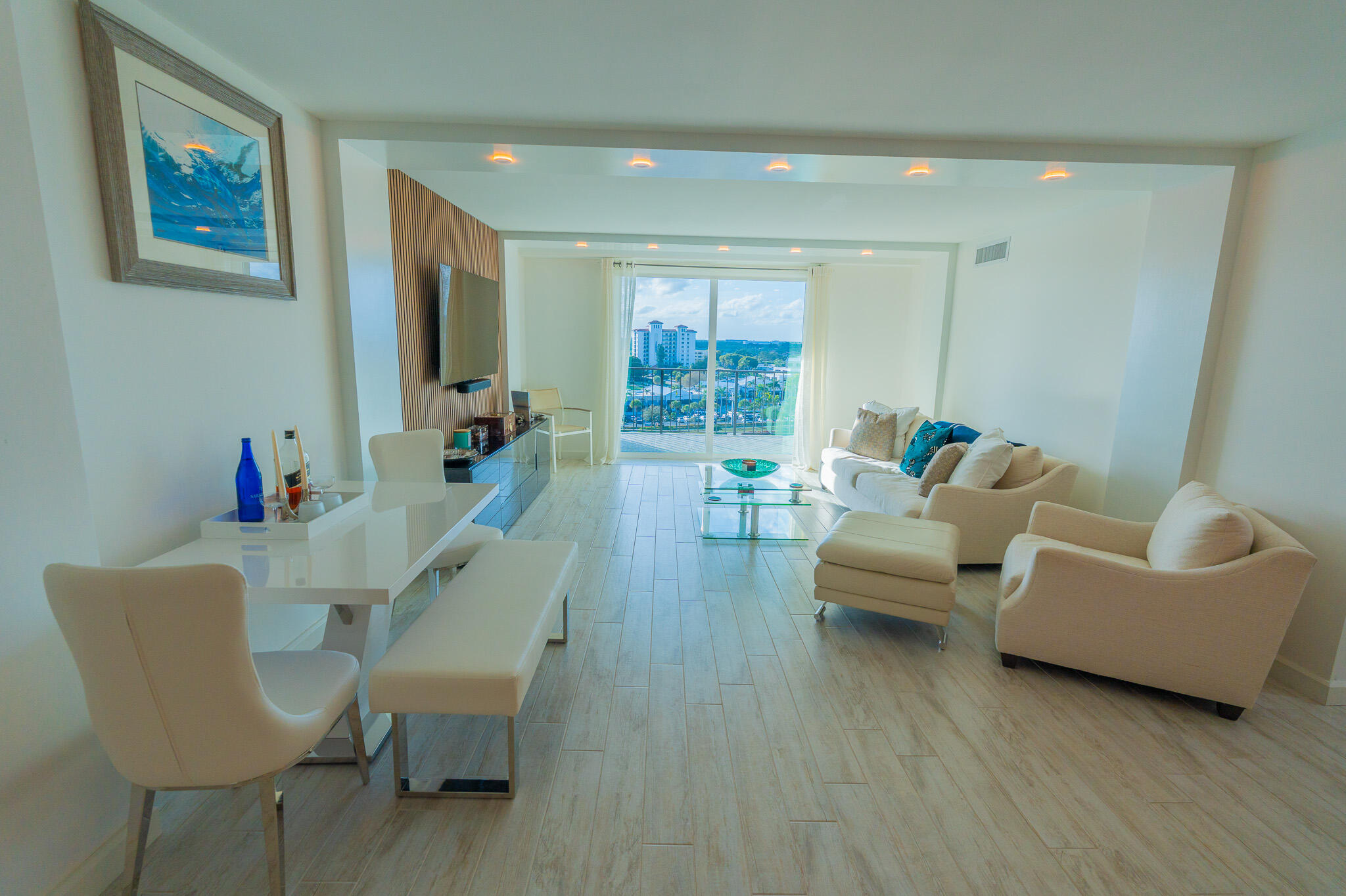 Open-plan living and dining room with neutral furnishings and a balcony overlooking the water.