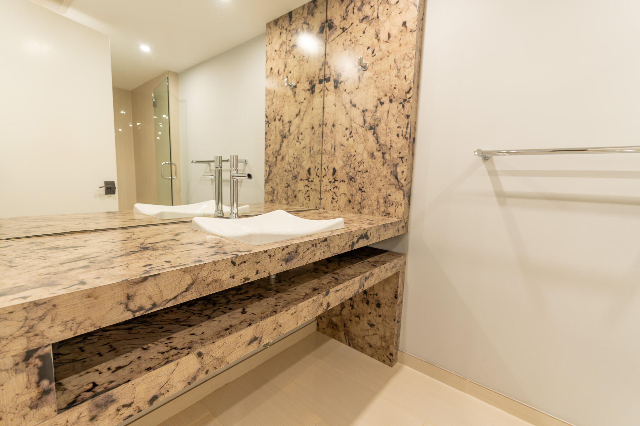 Bathroom vanity with a white vessel sink, patterned stone countertop and matching wall, and a large mirror.