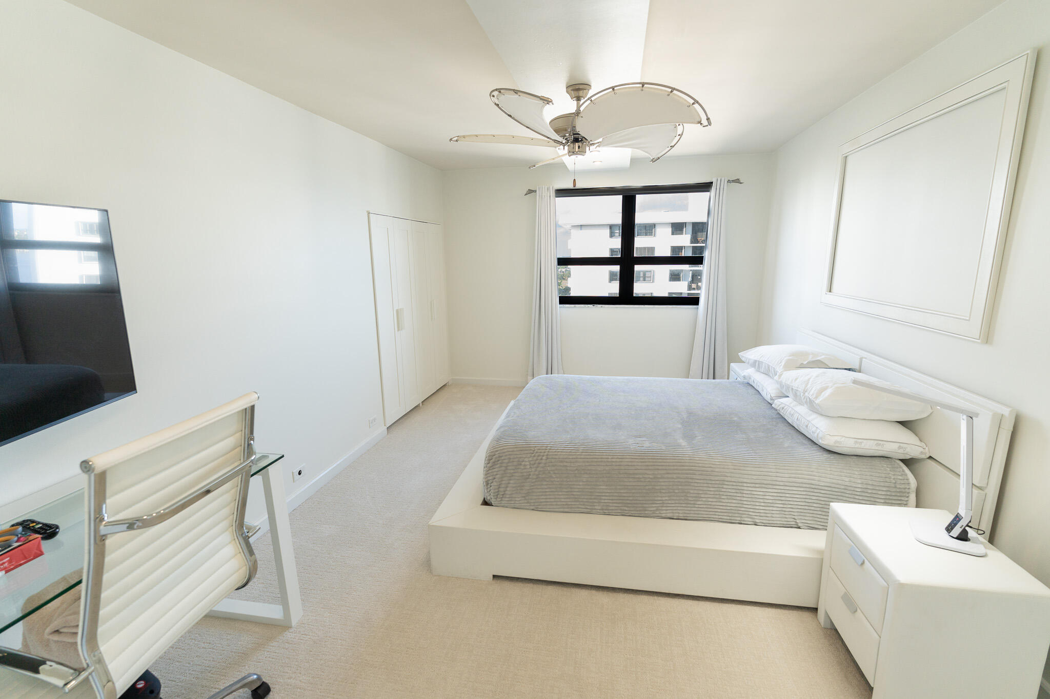 Bright bedroom with a low white bed, gray striped bedding, and a black-framed window.