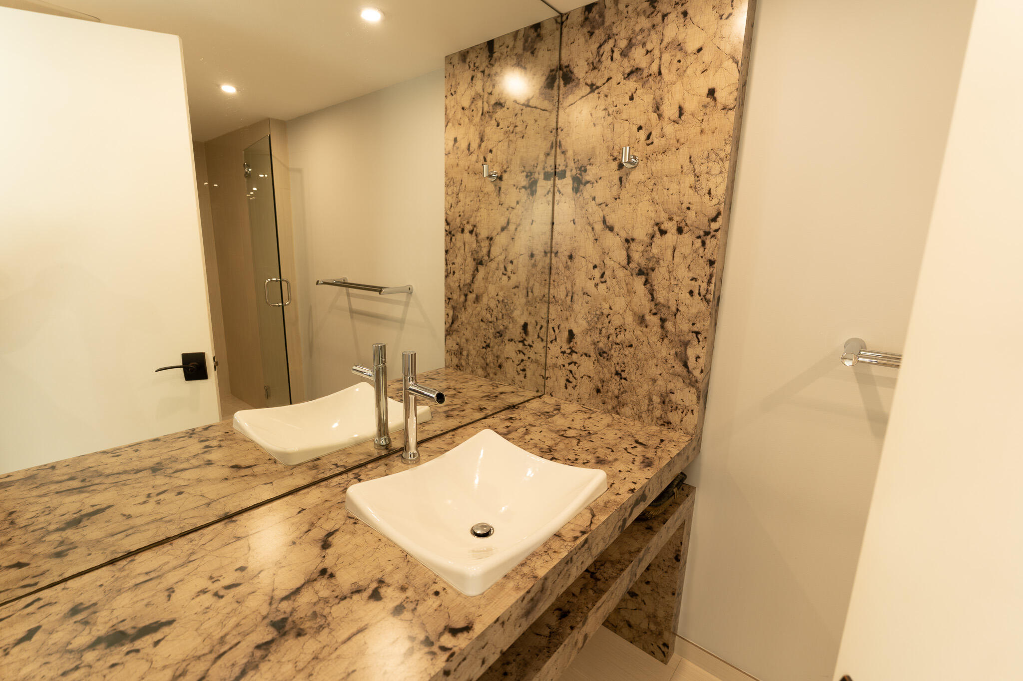 Bathroom vanity with a white vessel sink, dramatic patterned stone counter, and glass shower.