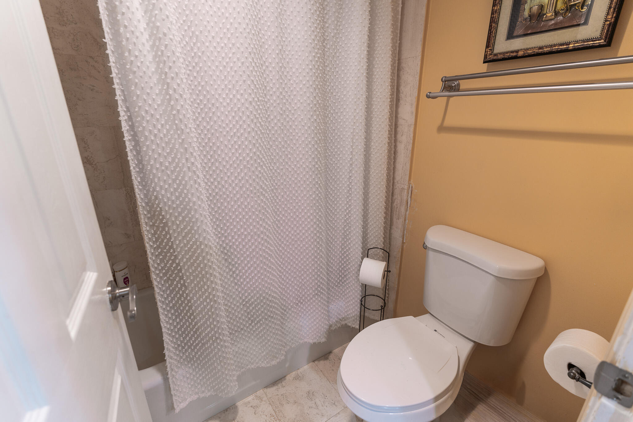 Bathroom with a textured white shower curtain, beige tile, and a white toilet.