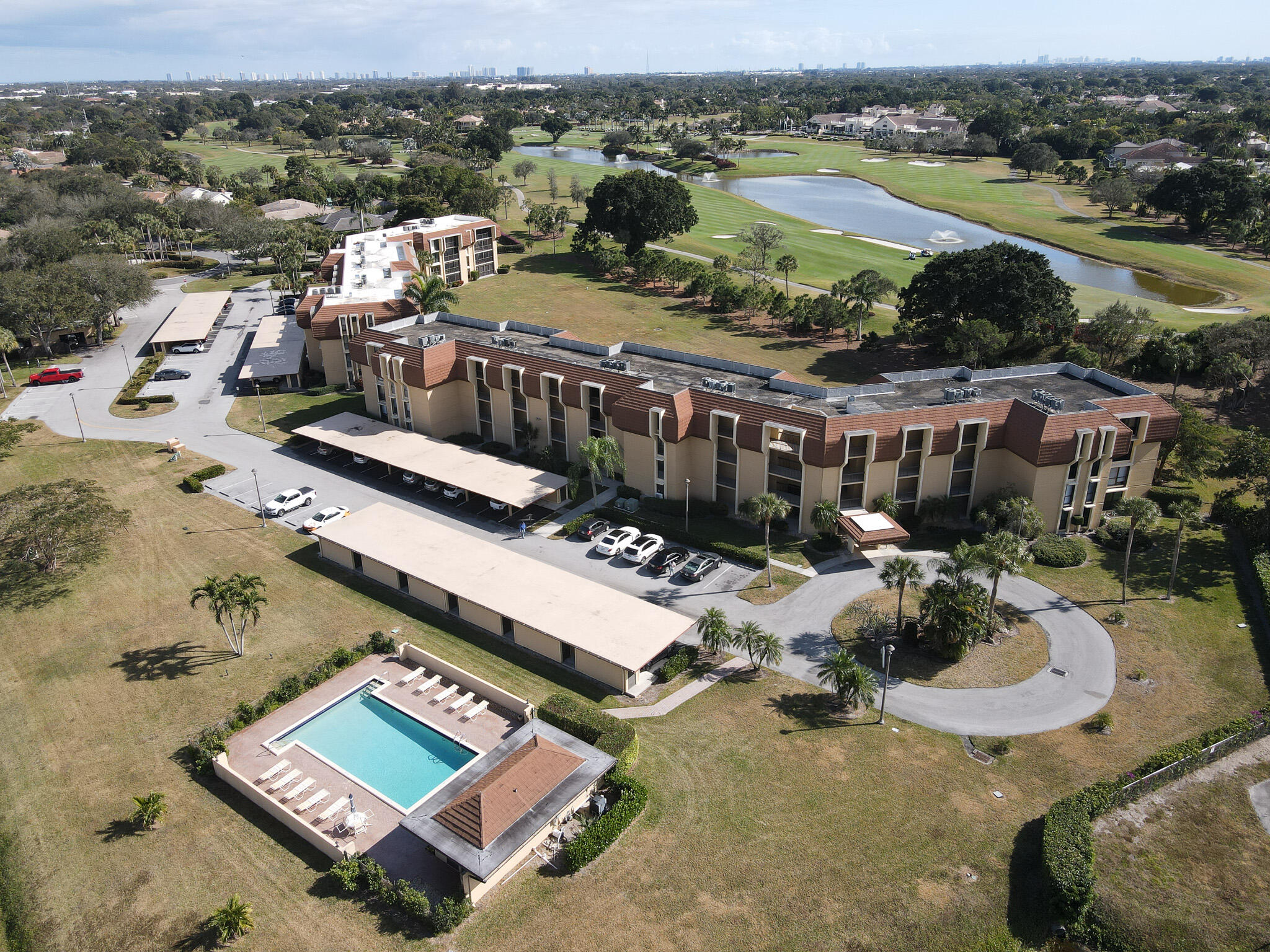Aerial view of a condominium complex with a pool beside a golf course and lake.