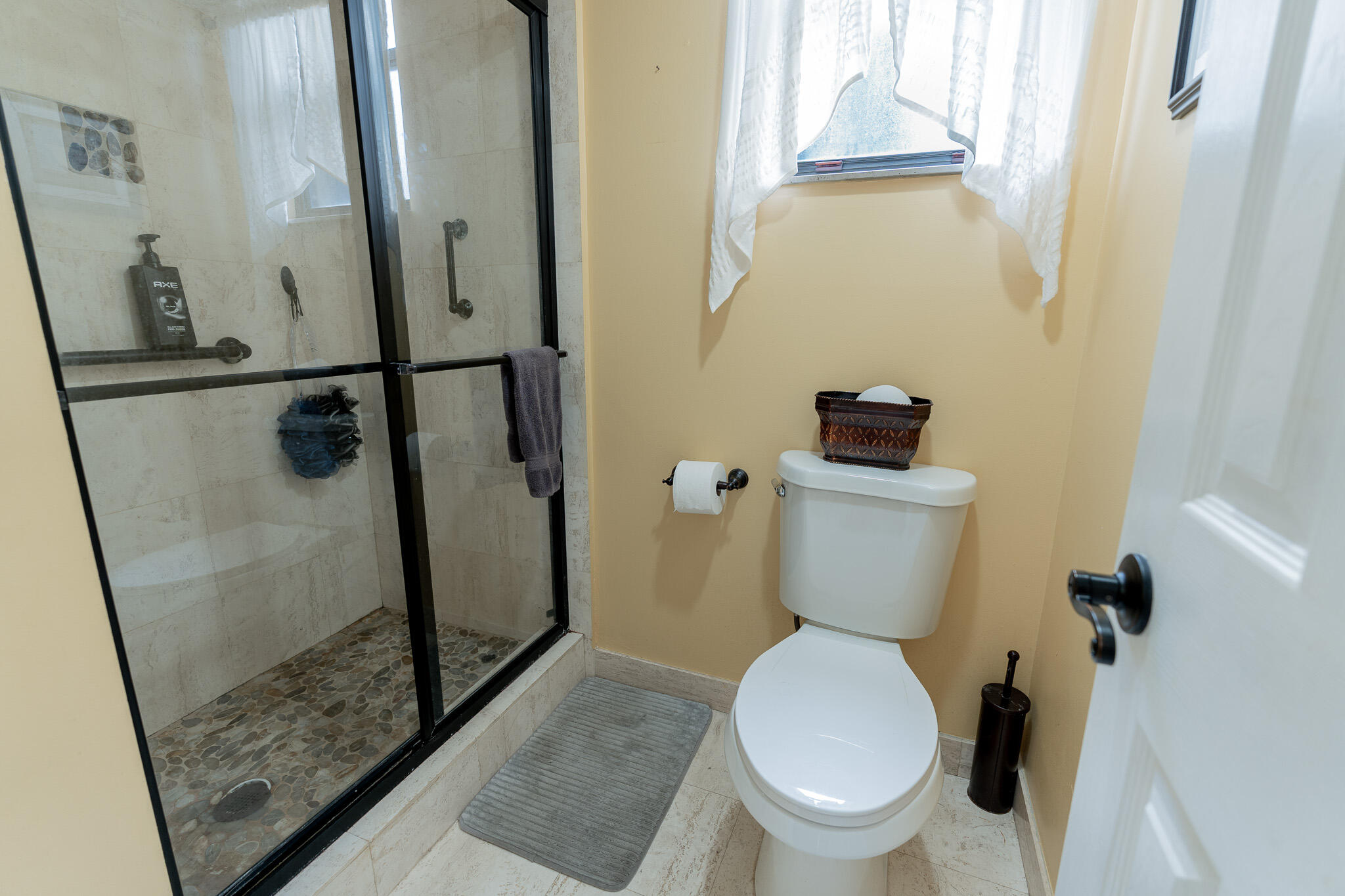 Bathroom with a glass-enclosed pebble-floor shower and white toilet.