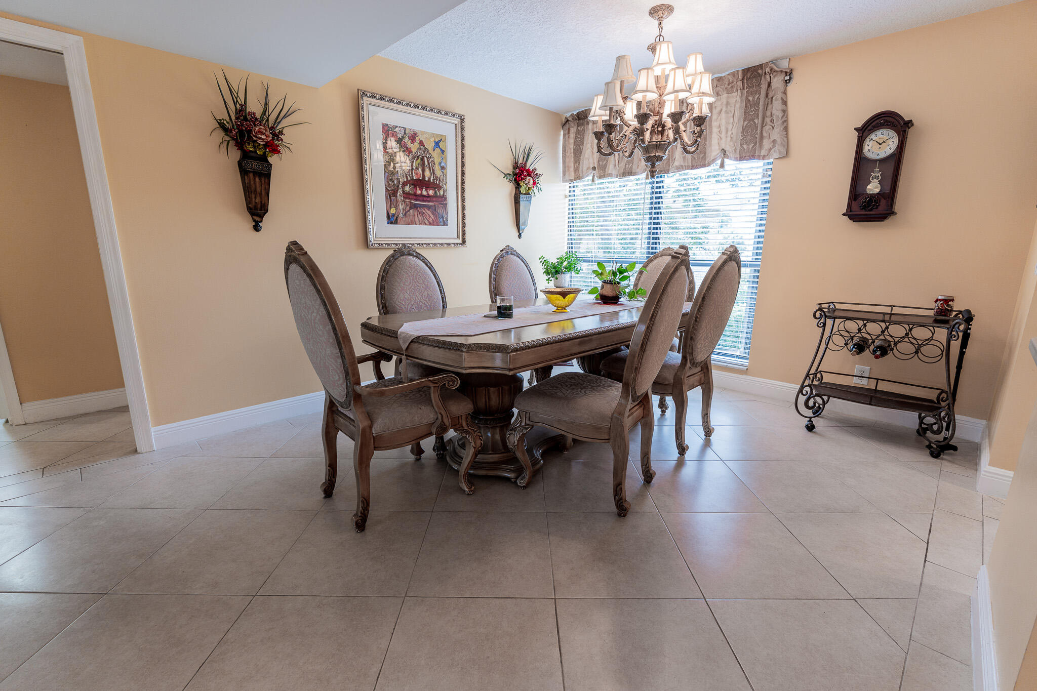 Dining room with a carved wooden table, upholstered chairs, chandelier, and bright window.