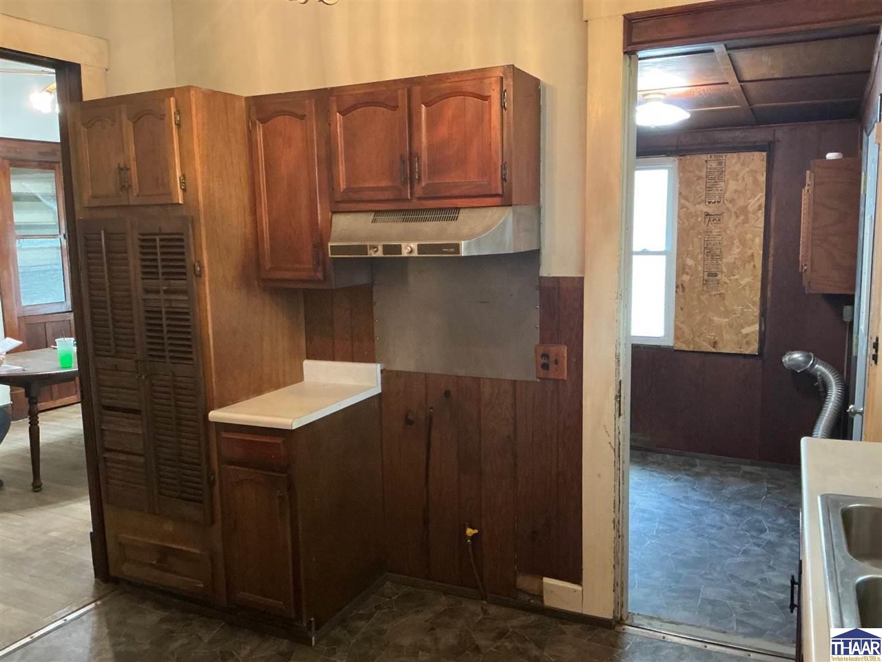 Kitchen with dark wood cabinets, a range hood, and an open doorway to an adjoining room.