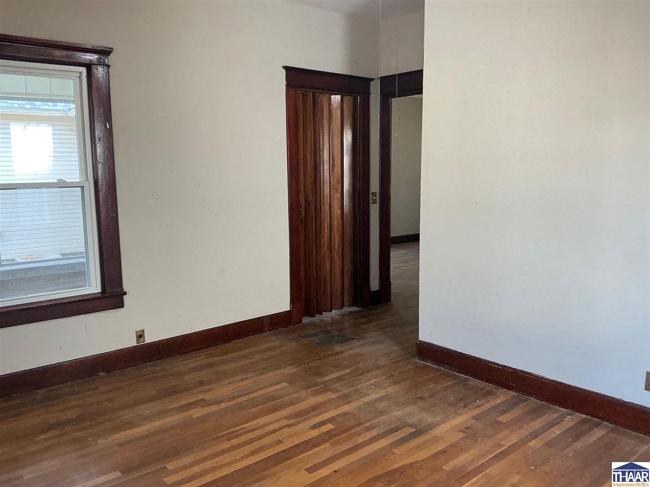 Empty room with hardwood floors and dark wood trim around the window and doorway.