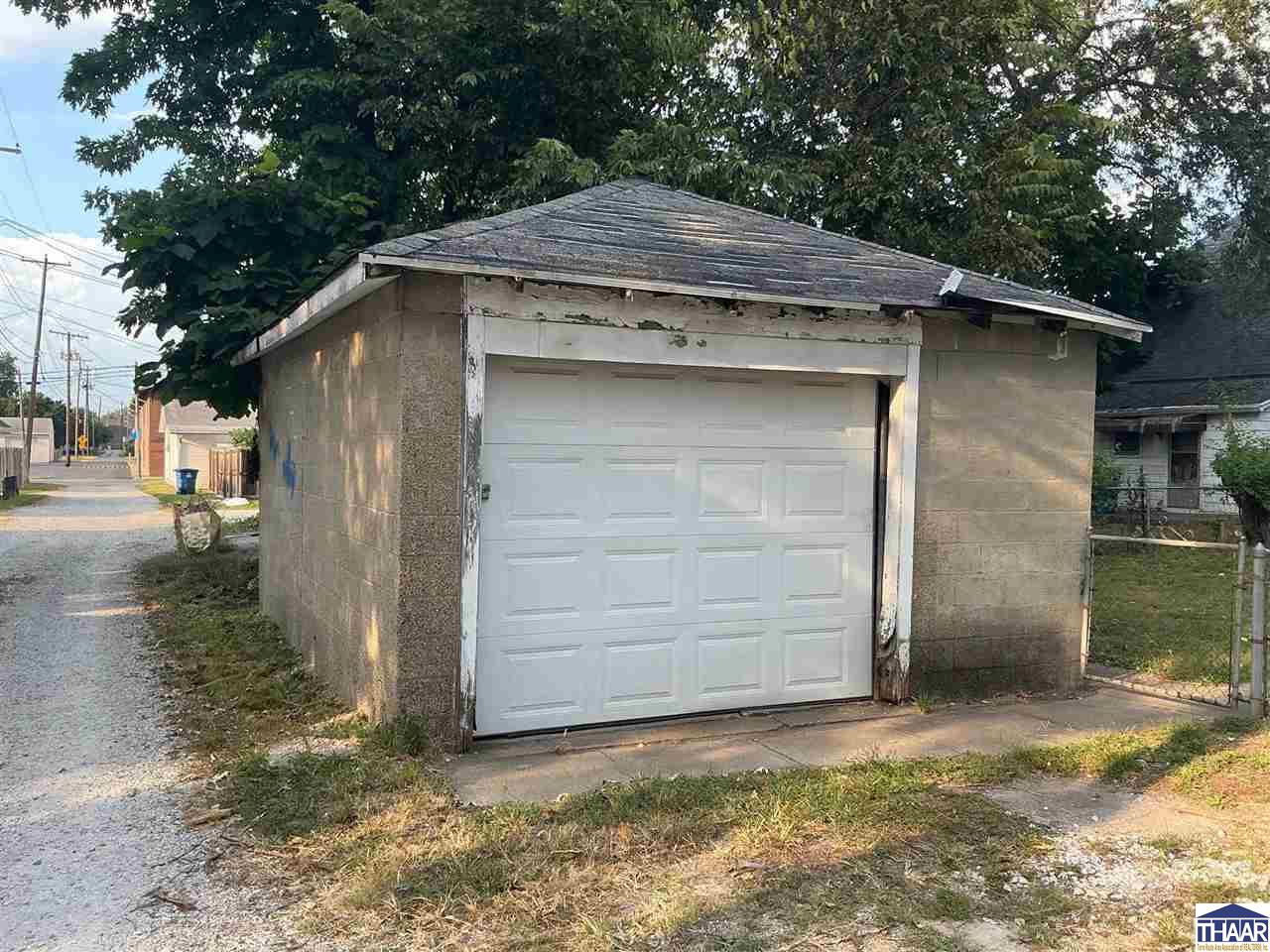Detached garage with a white paneled overhead door beneath mature trees.