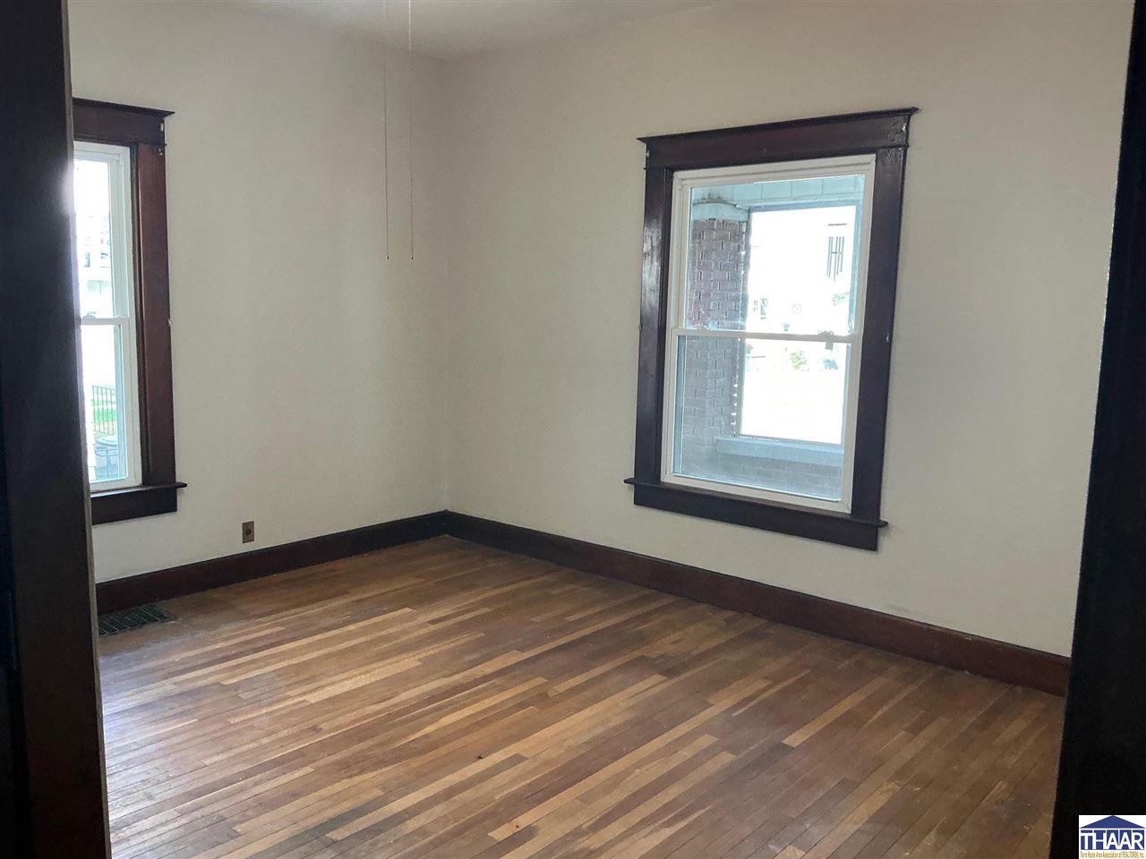 Empty room with polished hardwood floors, dark wood trim, and two windows.