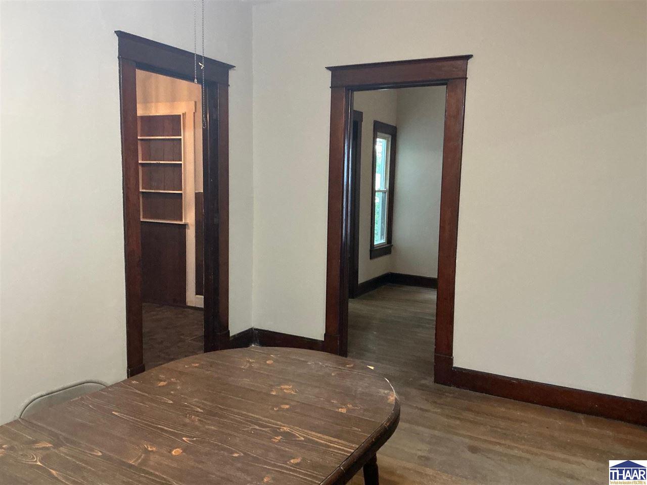 Interior with a dark wooden table, wide wood-trimmed doorways, and built-in shelving.