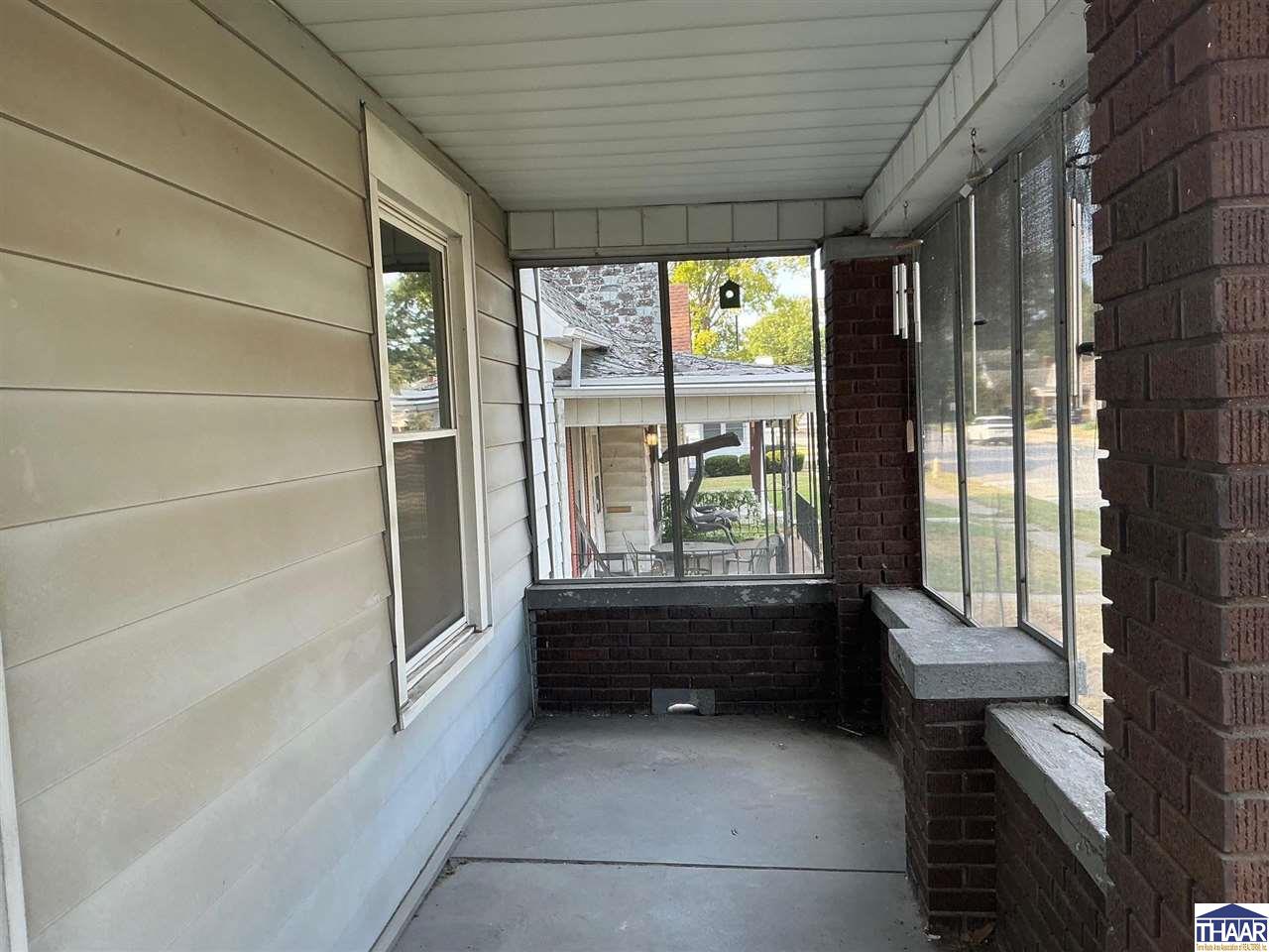 Enclosed front porch with white siding, large windows, and brick half-walls.