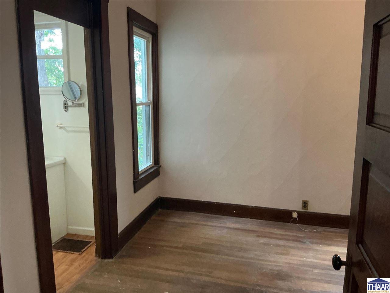 Empty room with wood flooring and dark trim, beside a bathroom doorway.
