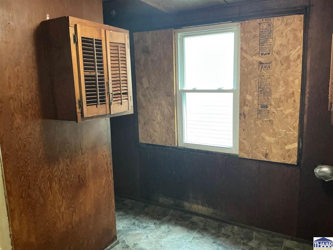 Unfinished room with exposed plywood walls, a louvered wooden cabinet, and a window.