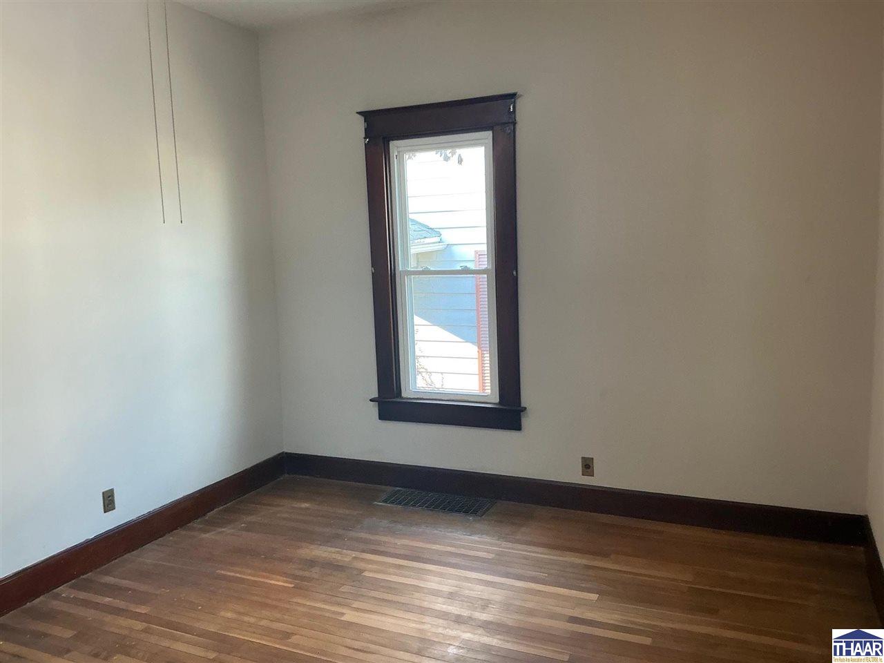 Unfurnished room with hardwood floors, dark wood trim, and a tall window.
