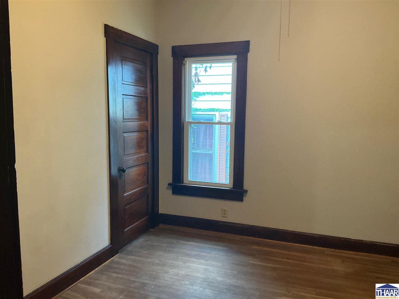 Empty room with dark wood trim, a paneled door, one window, and hardwood floors.