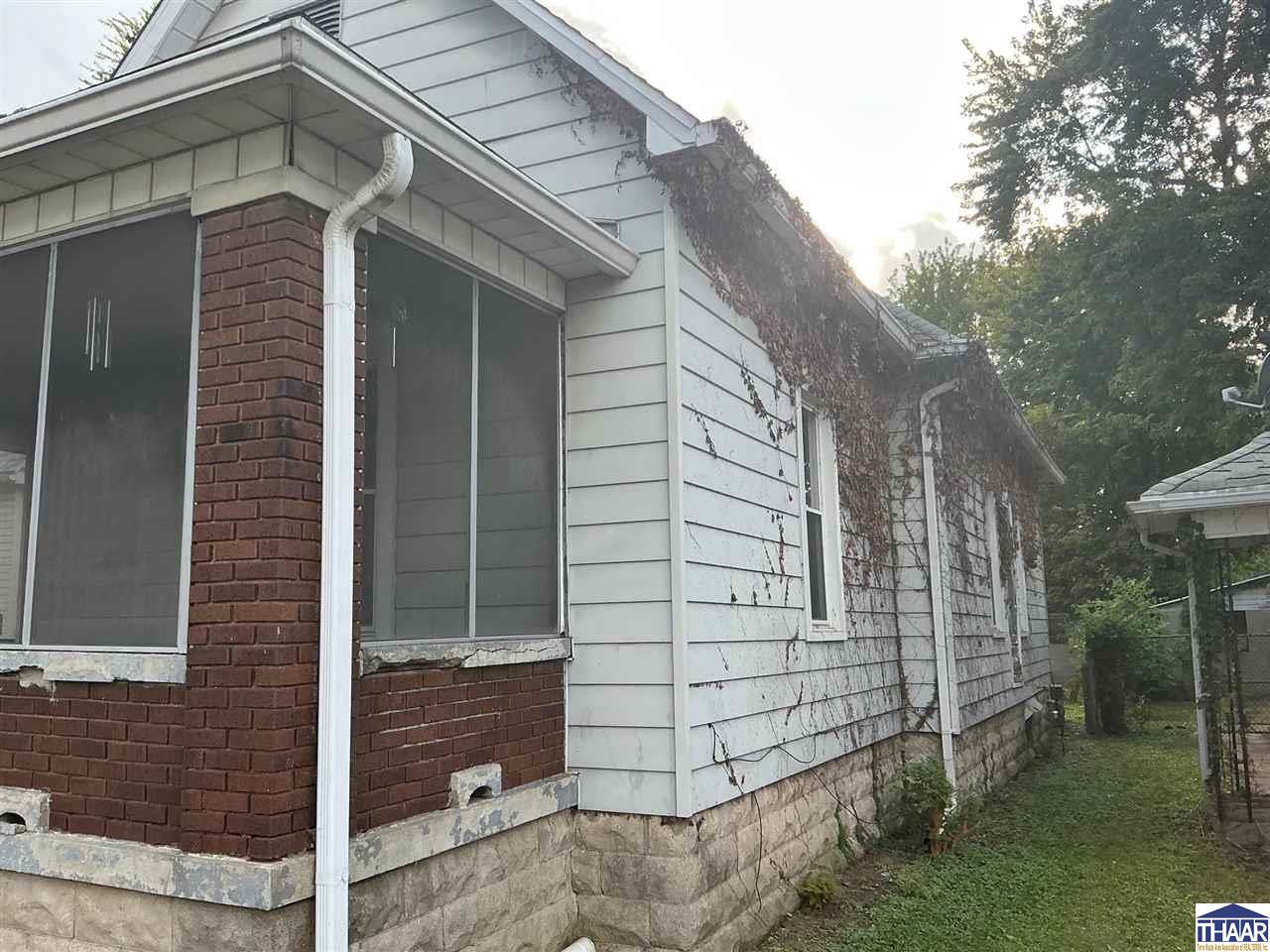 House exterior with a brick porch, screened windows, and ivy climbing the white siding.