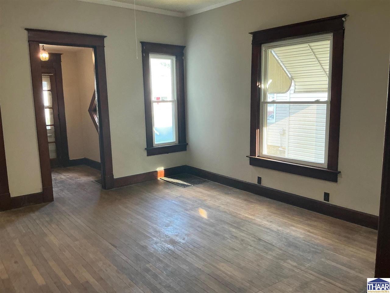 Vacant living room with hardwood floors, dark wood trim, and two tall windows.