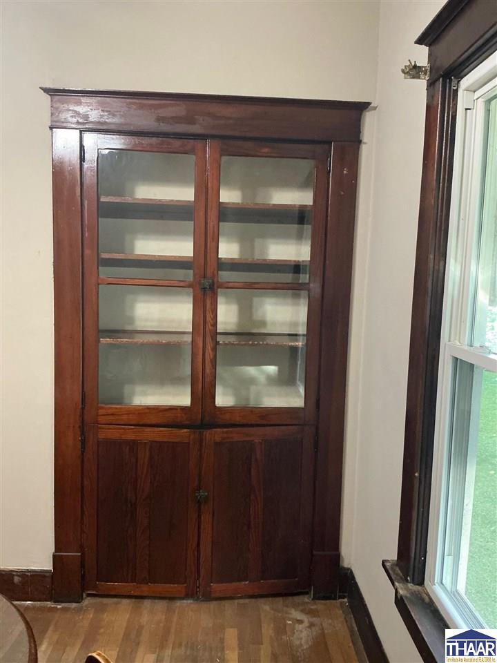Built-in dark wood cabinet with glass-front doors beside a tall window.