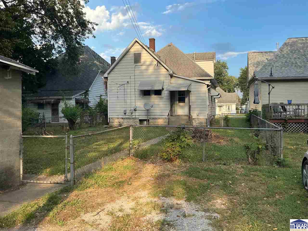 Rear of a light-colored gabled house behind a chain-link fence and grassy yard.