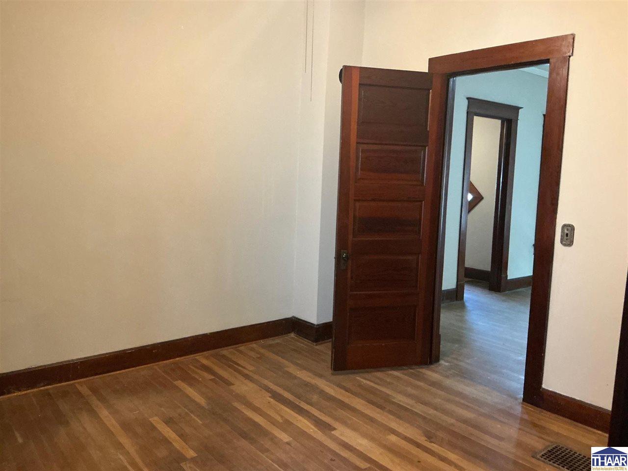 Empty room with hardwood floors and dark wood trim, looking through an open paneled door.