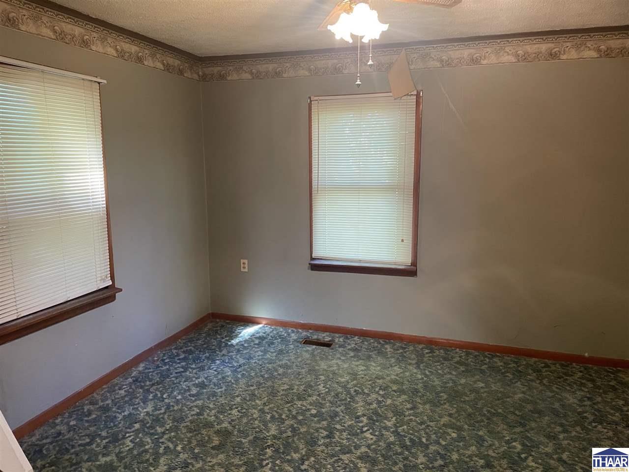 Empty room with patterned carpet, two windows with blinds, and ornate ceiling trim.