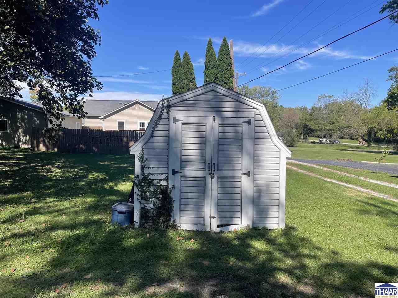 Gray gambrel-roof shed with double doors on a grassy residential lot.
