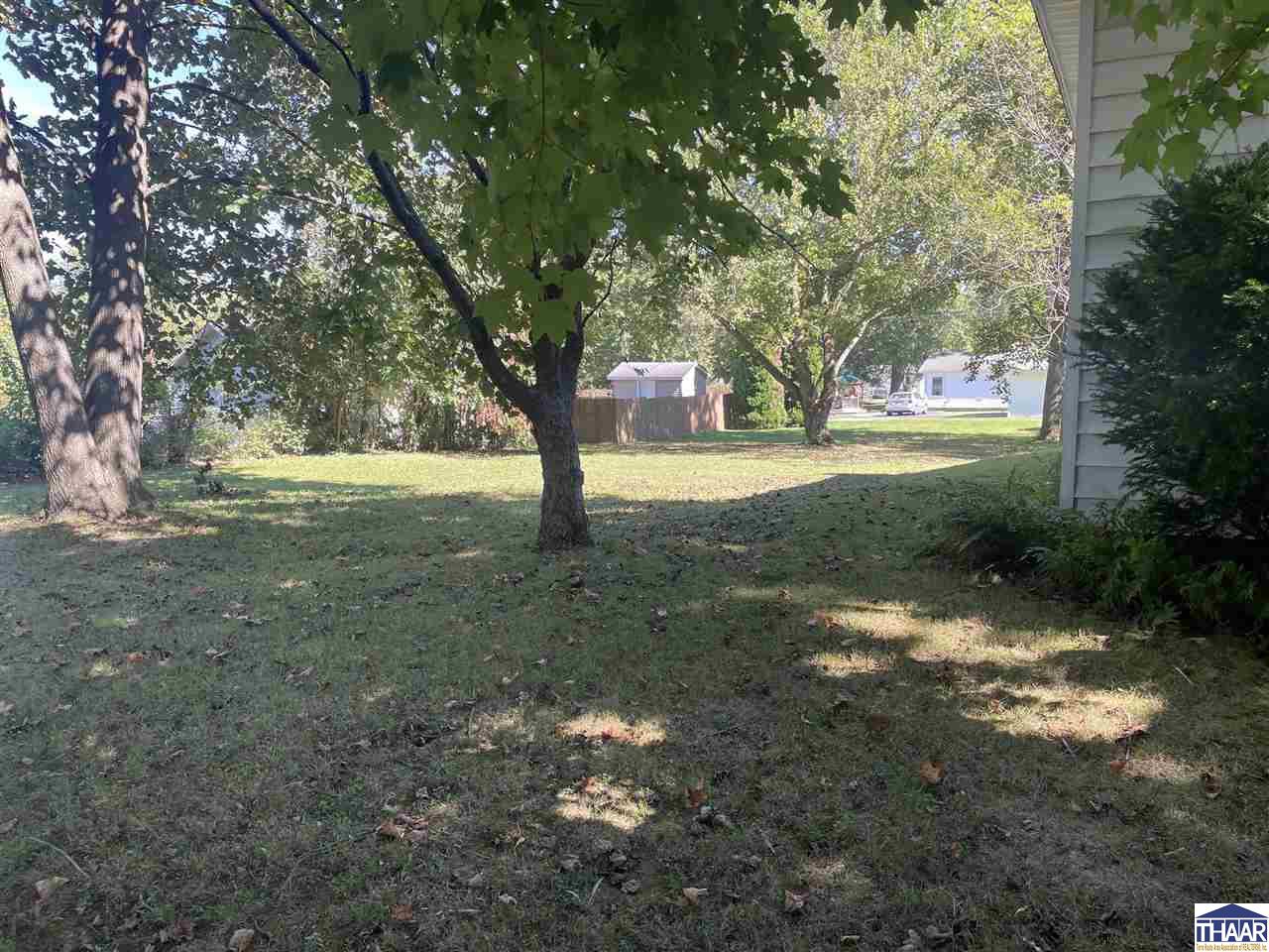 Backyard with mature shade trees, a lawn, and a wooden fence.