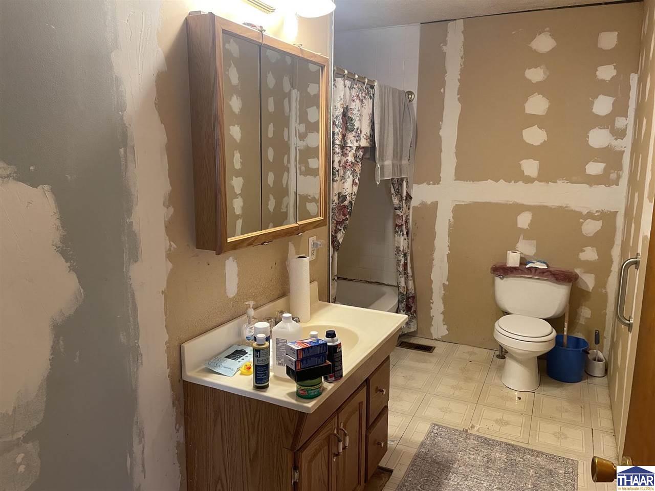 Bathroom with a wood vanity, tub and toilet; drywall walls are unfinished with visible patches.