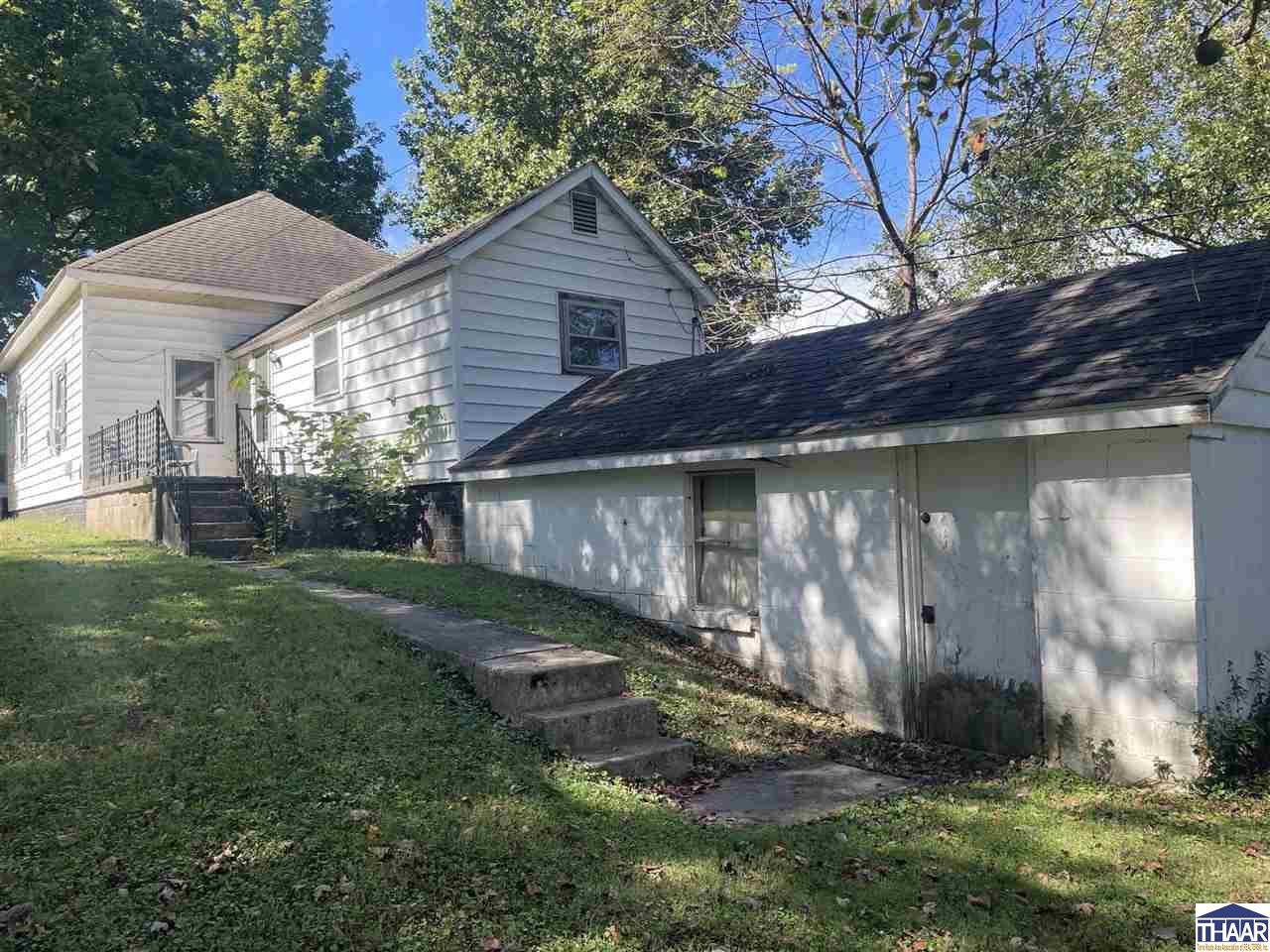 Light-sided house with a gabled upper section and long attached garage beside a grassy yard.