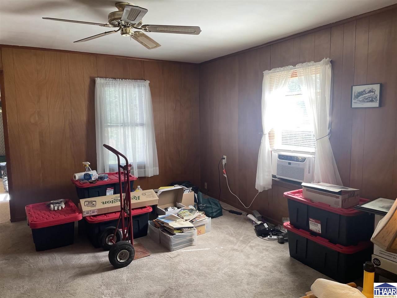Carpeted room with wood-paneled walls, a window air conditioner, and scattered storage bins and boxes.
