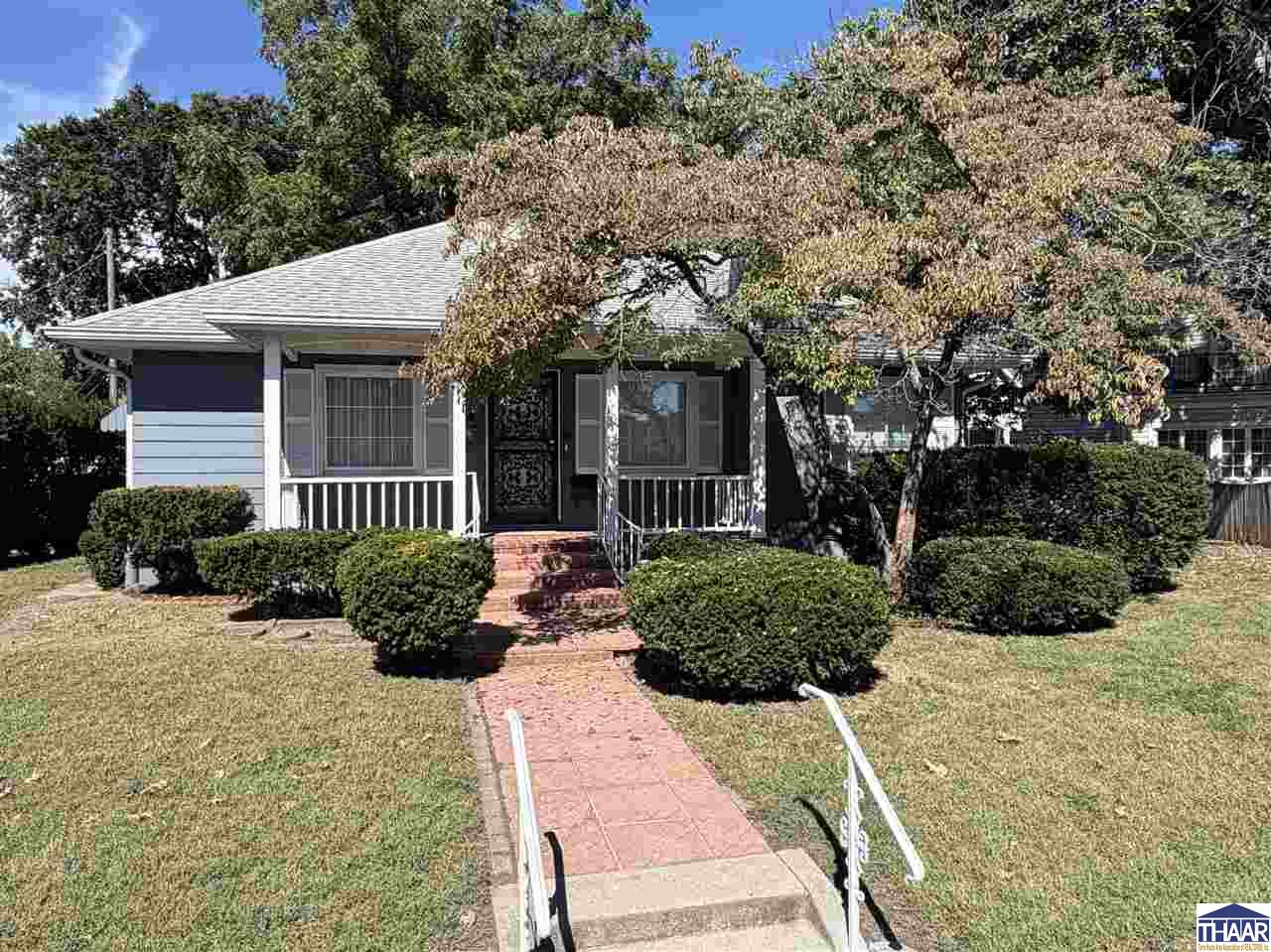 Single-story house with a covered porch, trimmed shrubs, and a brick walkway to the entrance.
