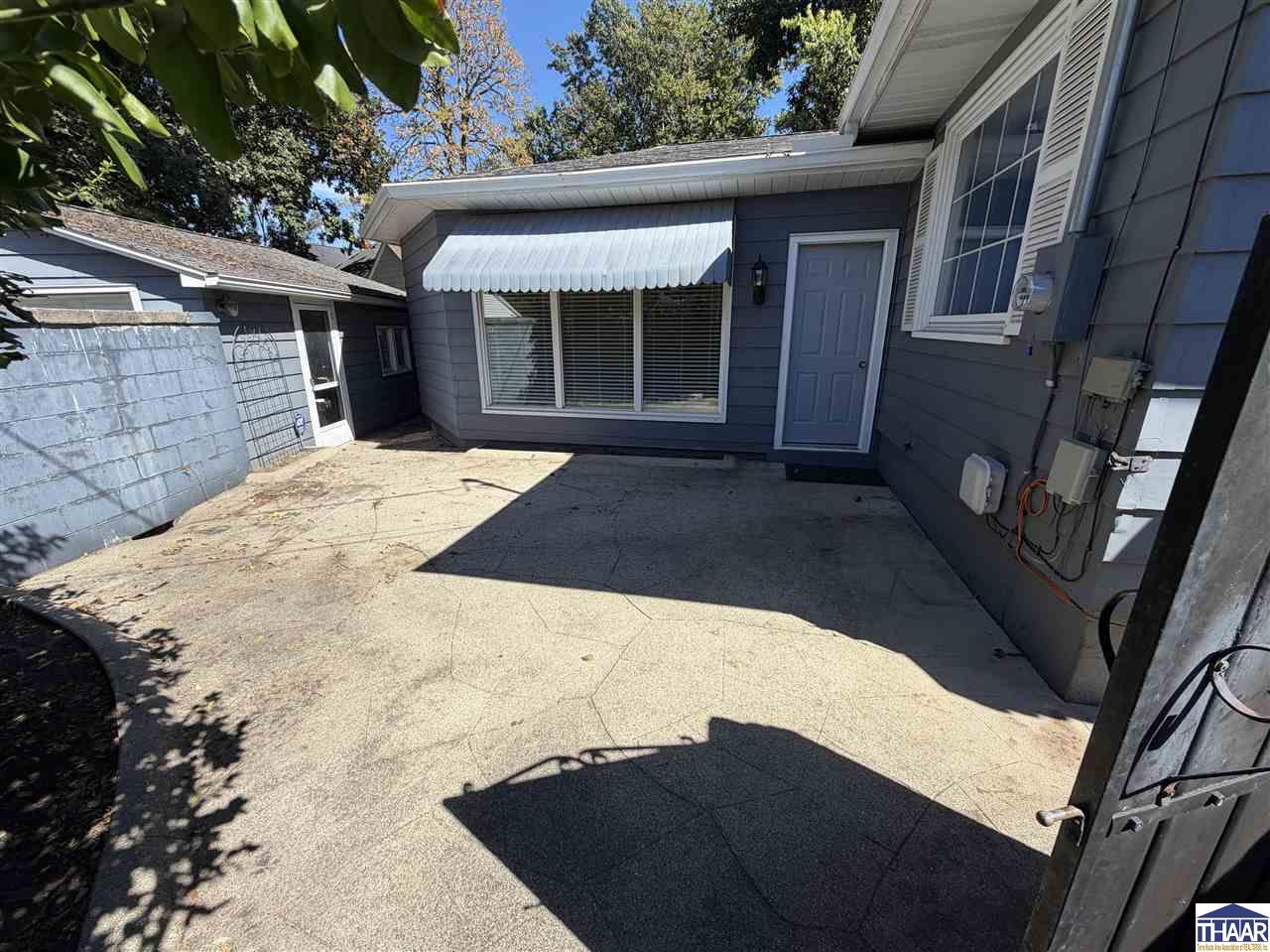Concrete courtyard beside a blue-gray house with a white window awning and blue door.