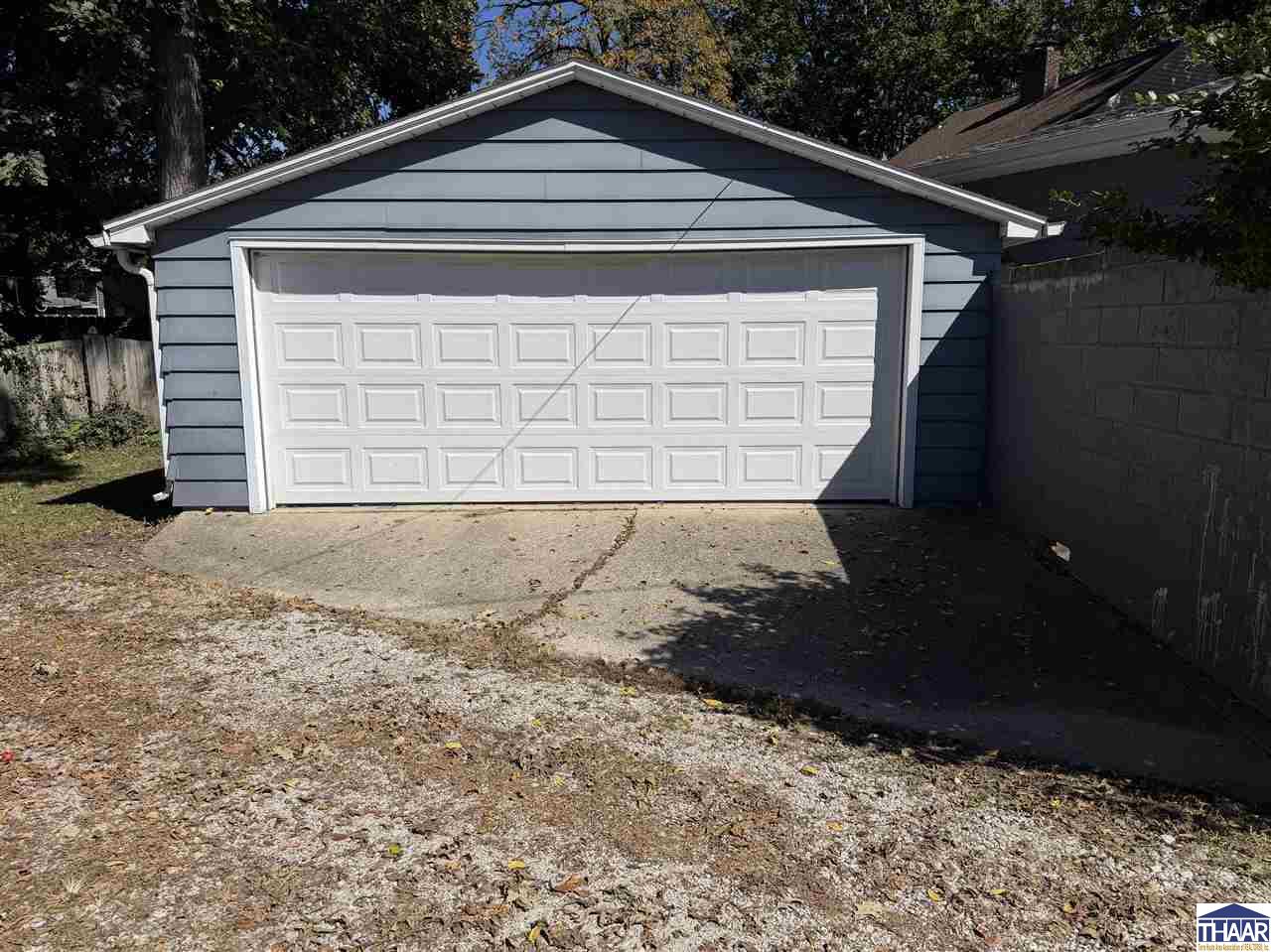 Blue-gray detached garage with a white double door beside a gravel driveway.