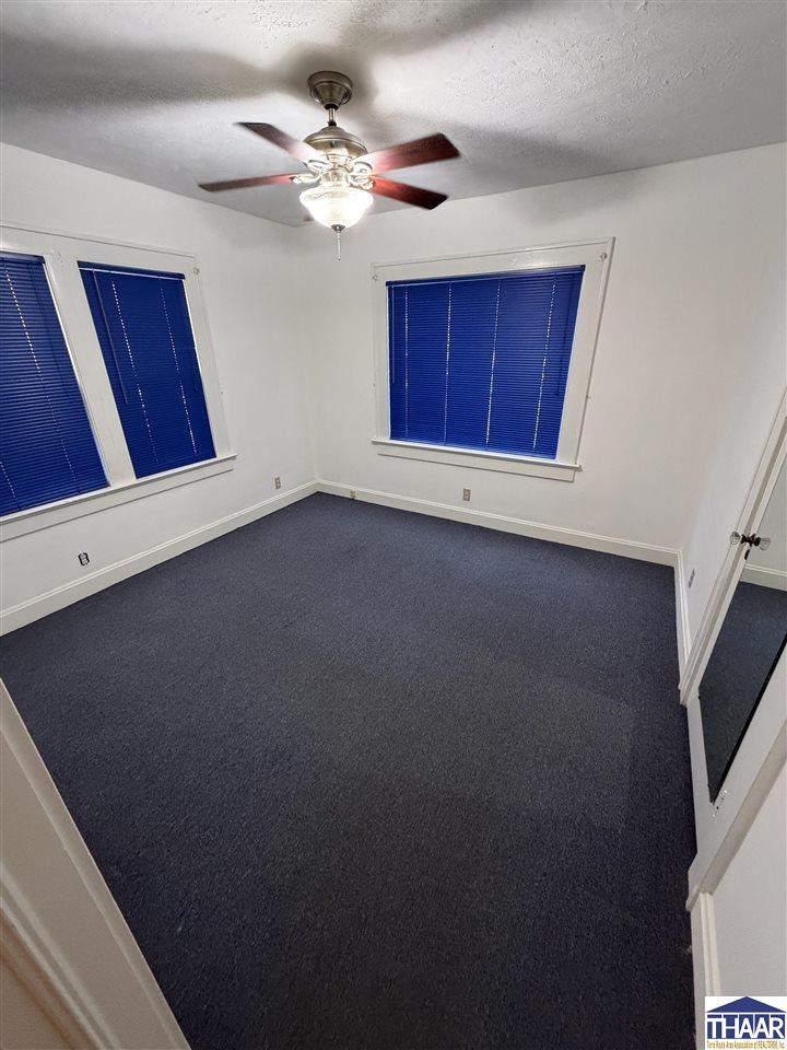 Empty carpeted room with blue window blinds and a lit ceiling fan.