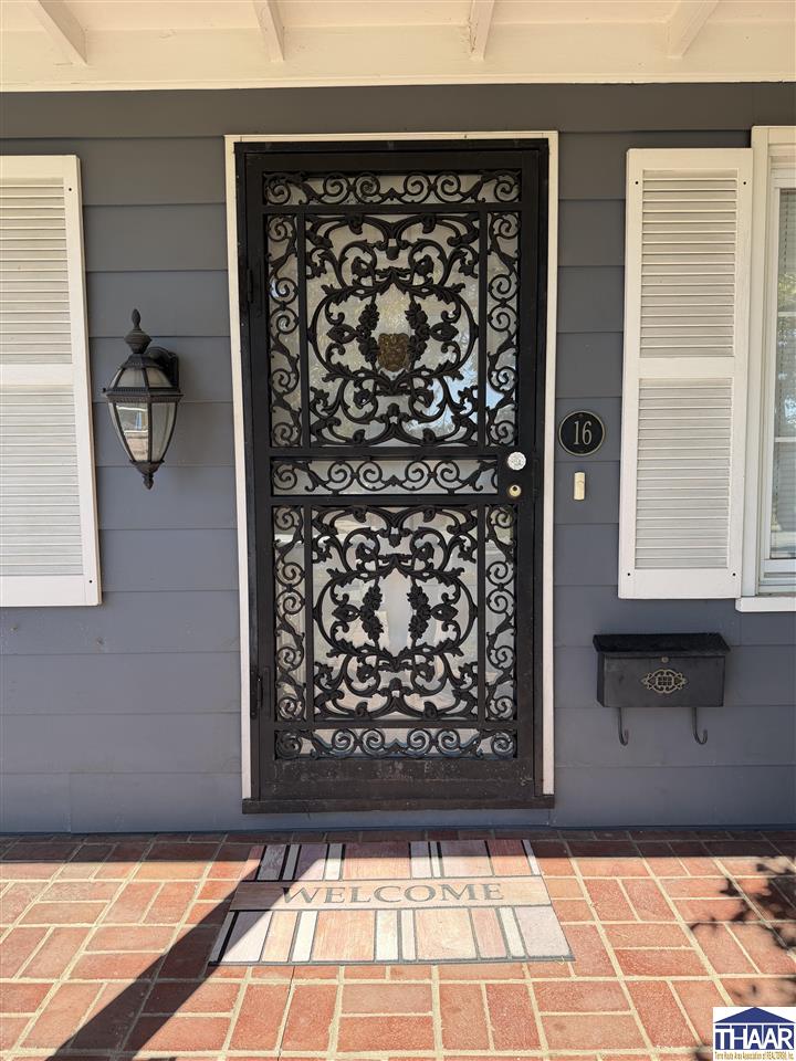 Front entrance with an ornate wrought-iron door, white shutters, and brick porch.