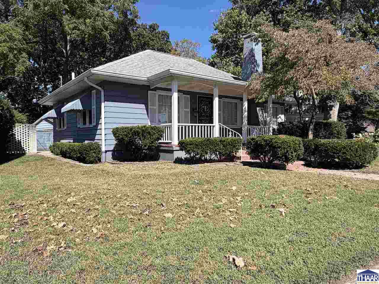 Blue single-story home with a covered porch, white railings, and trimmed shrubs along the front lawn.
