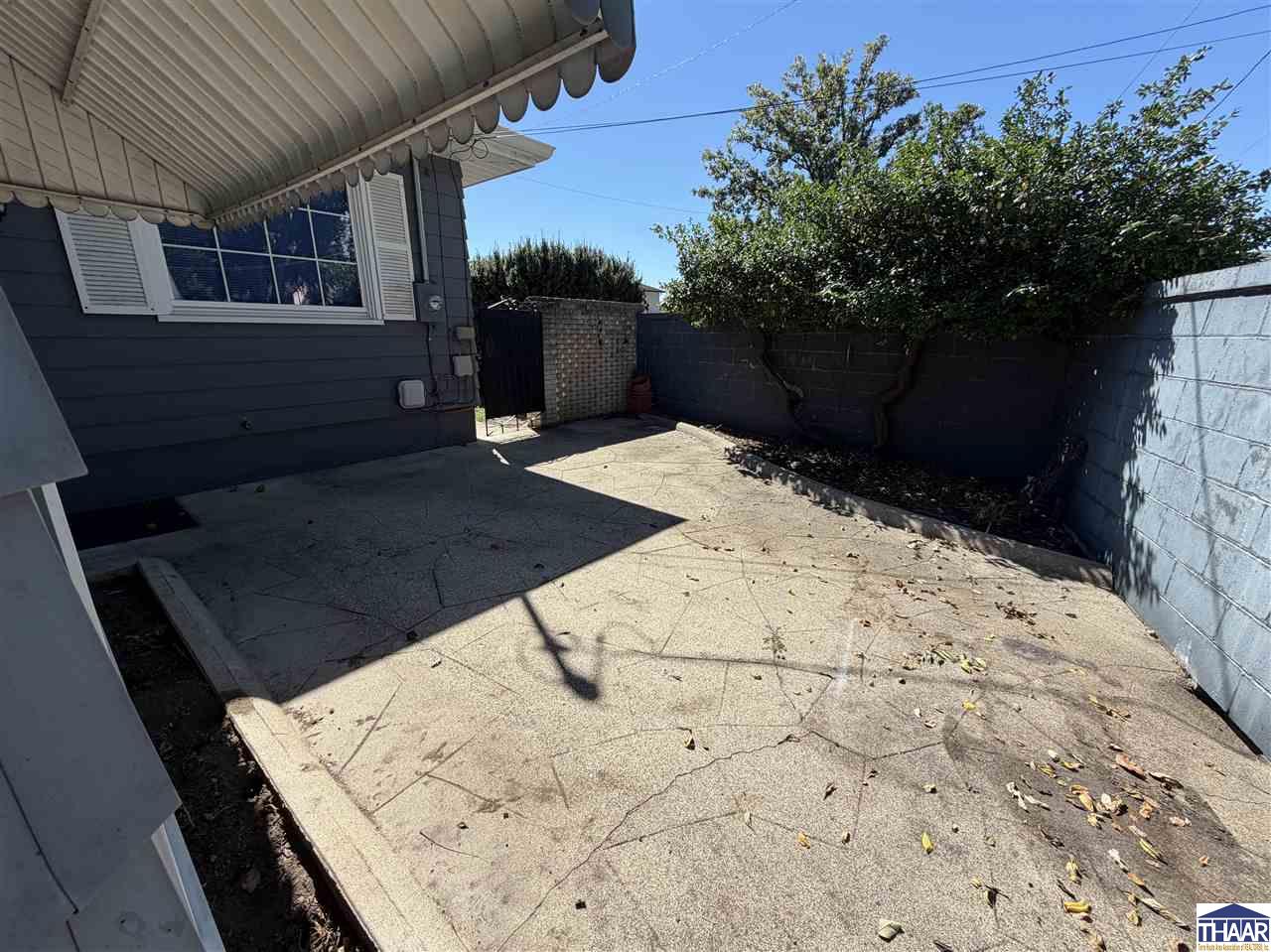 Concrete patio beside a dark-sided house, enclosed by block walls and shaded by a striped awning.