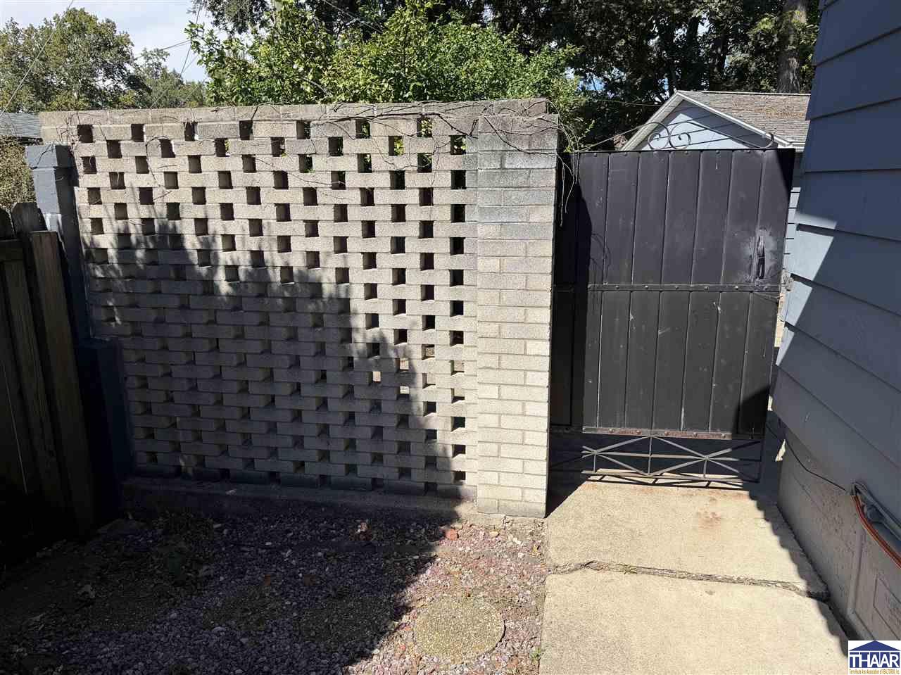 Side-yard walkway leading to a black gate beside a patterned concrete block wall.