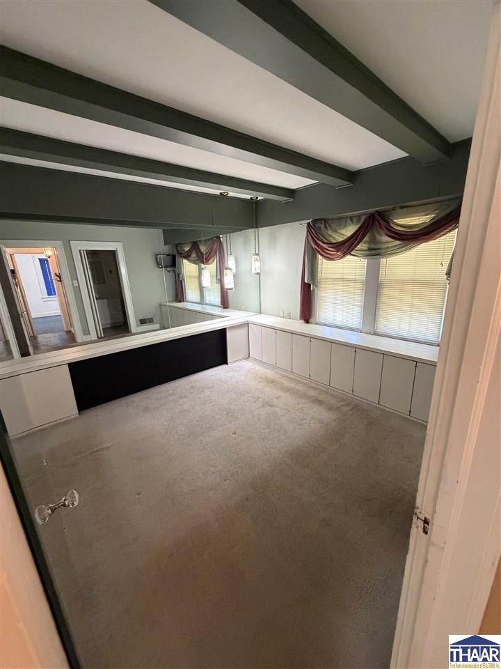 Vacant mirrored room with dark ceiling beams, carpet, and built-in window cabinets.