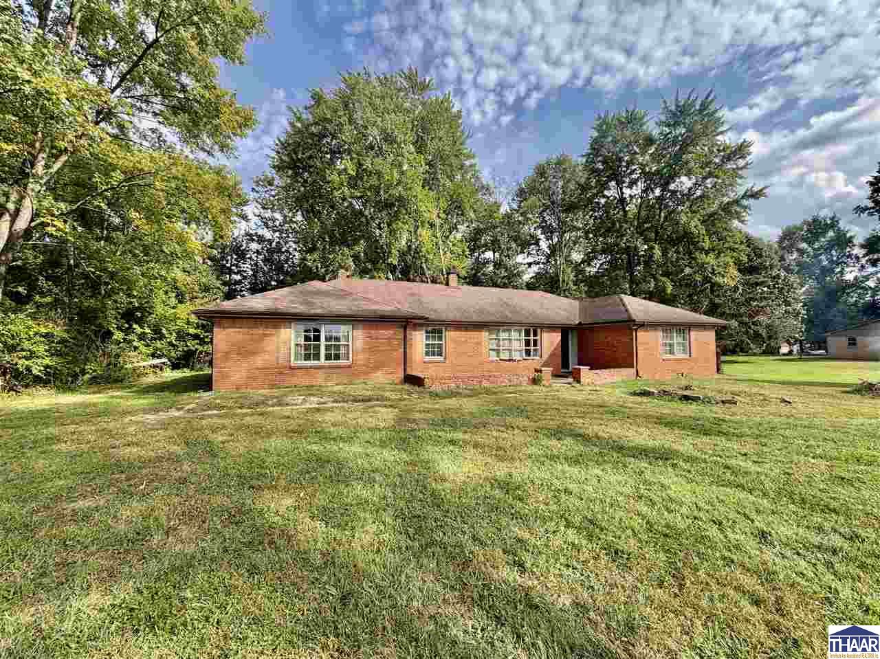 Red brick ranch house viewed from the rear, with a broad lawn and mature trees.