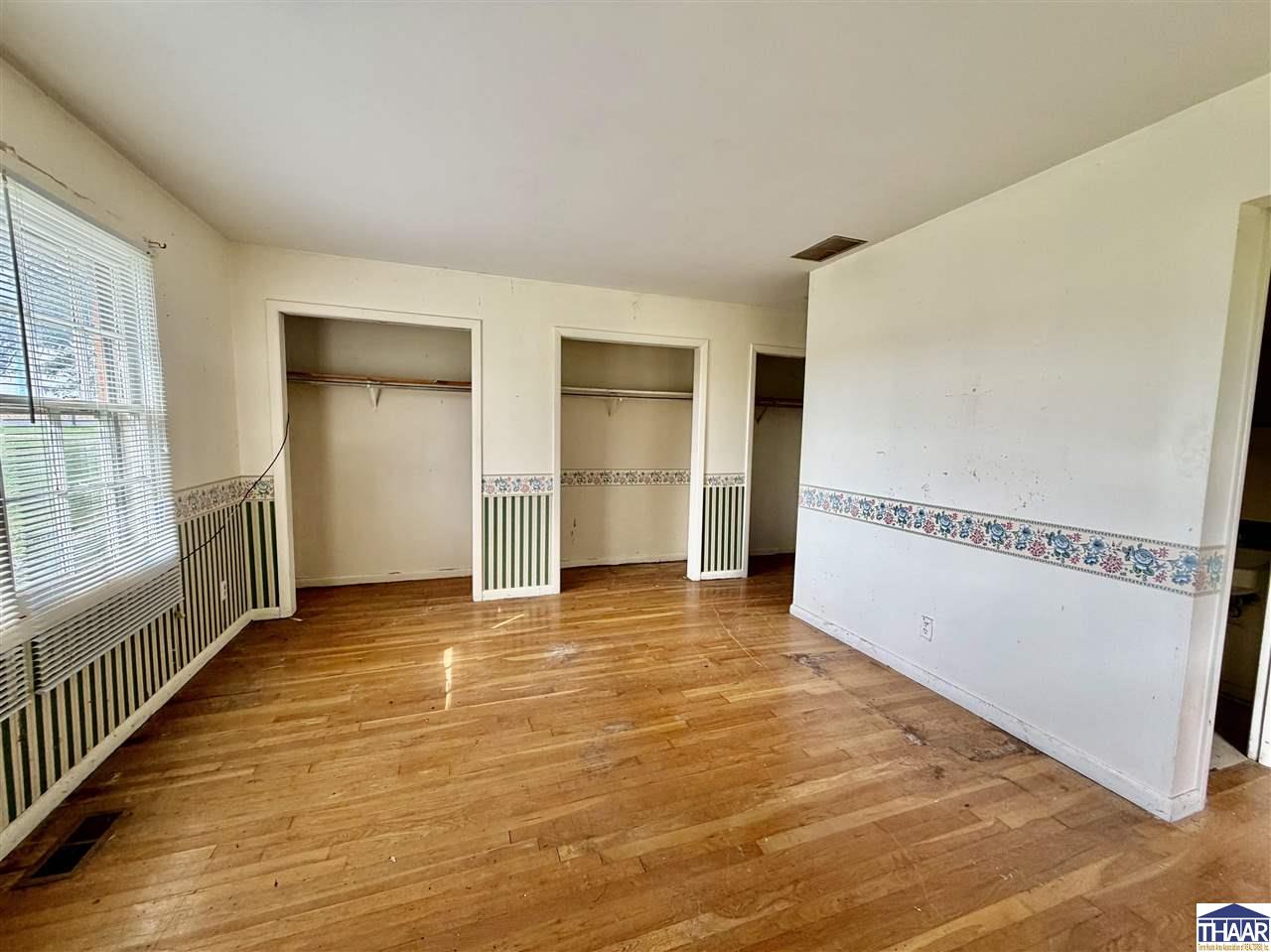 Empty bedroom with hardwood floors, three open closets, and striped wainscoting with a floral border.